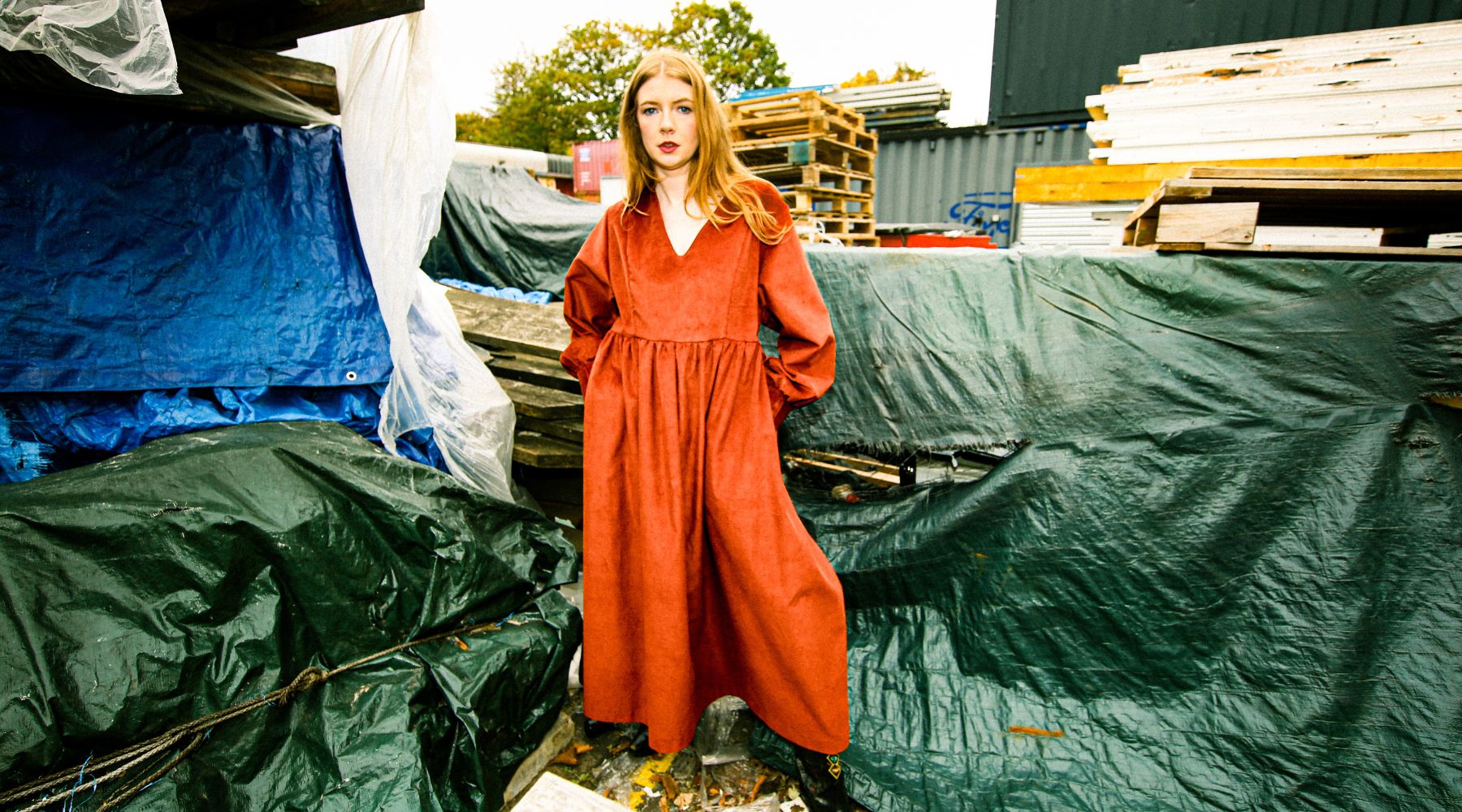 woman wearing a red maxi dress in the industrial estate, surrounded by blue plastic sheets
