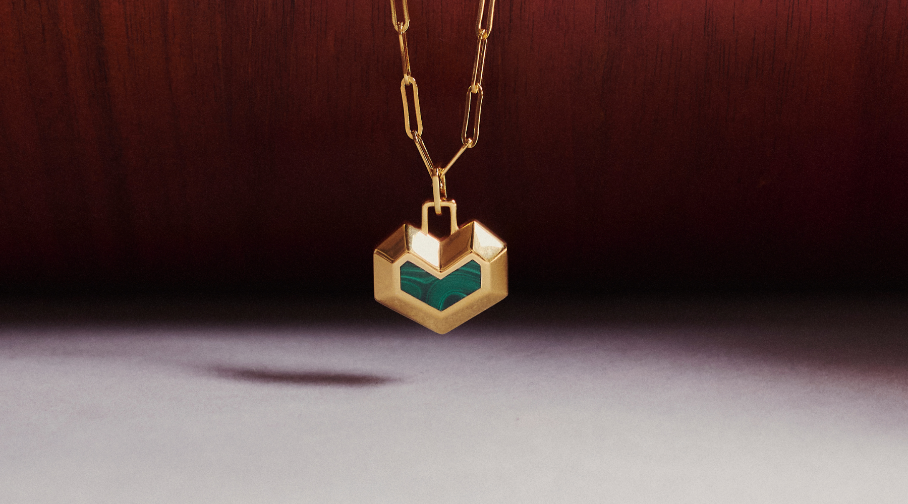 gold necklace with a heart shaped pendant and a green stone against a wooden background