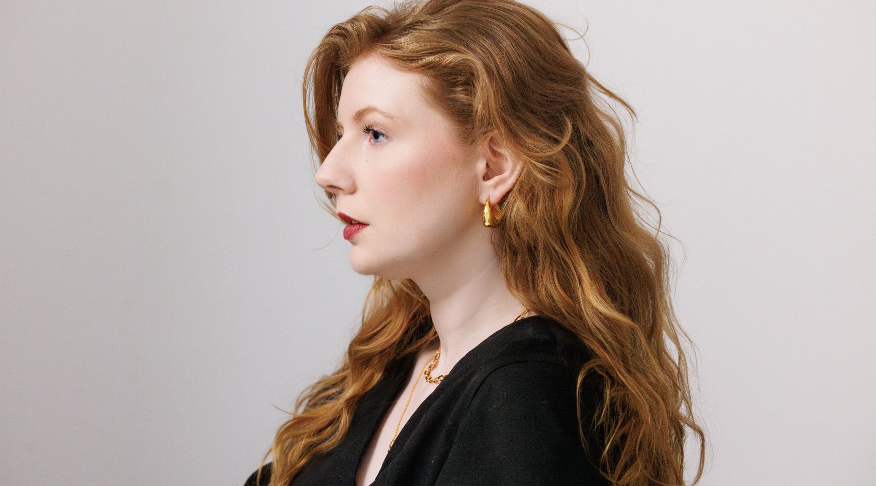 woman with red long hair wearing black top and gold earrings