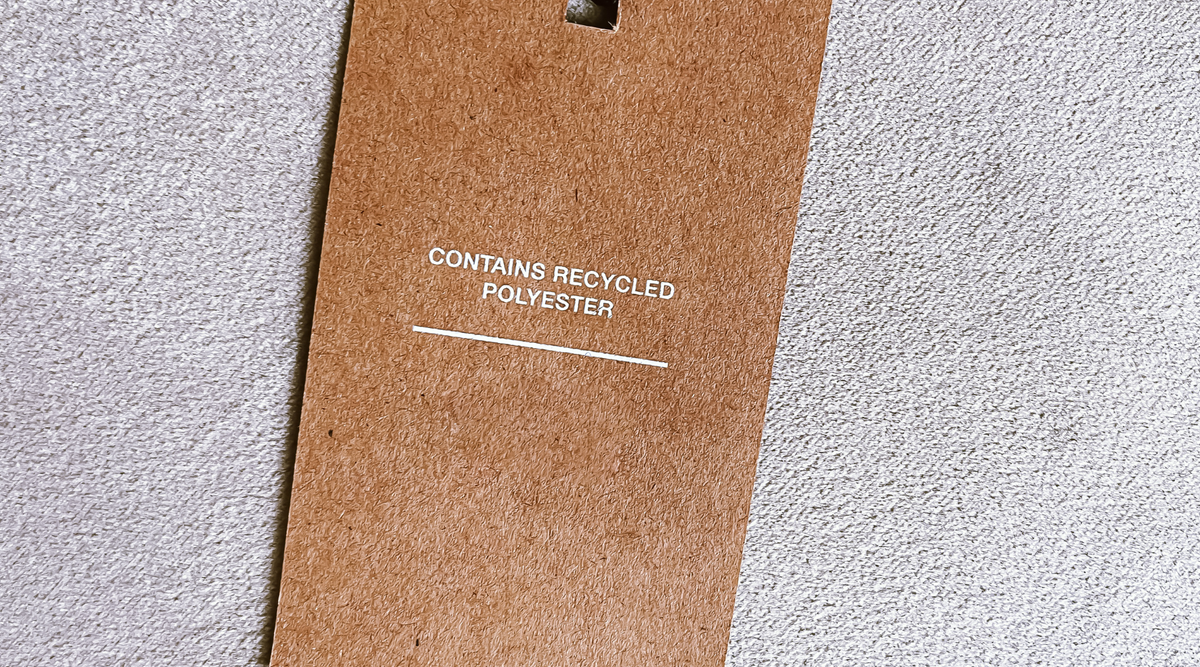 brown swing tag reading contains recycled polyester, on a off white background