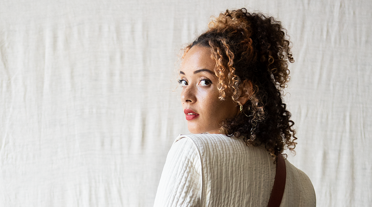 woman with orange curly hair turning around to look at the camera against a white background