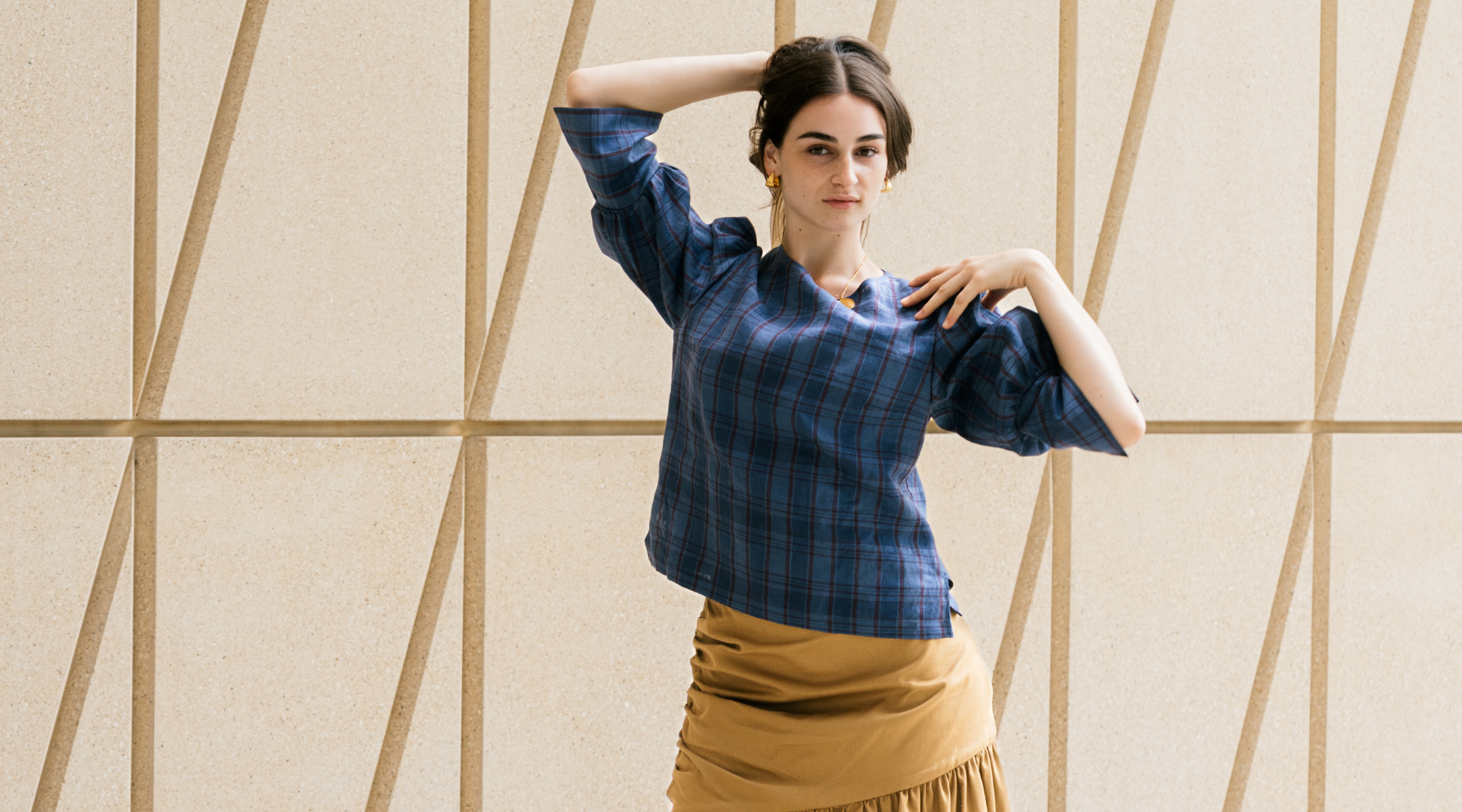 woman pulling her dark hair back wearing a navy check top looking at the cameraat