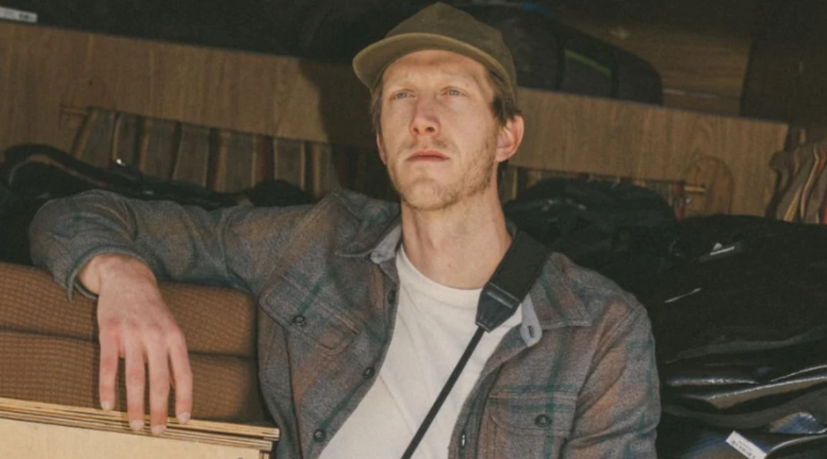 a man wearing a cap, white tshirt and a plait shirt looking at the distance in an urban background