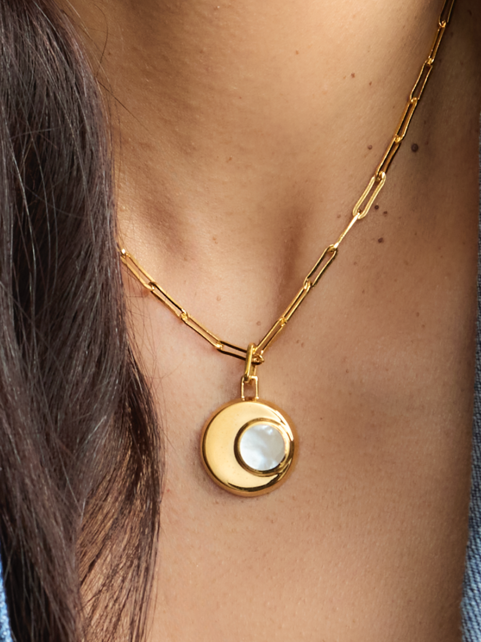 Gold necklace with a circular pendant worn by a person