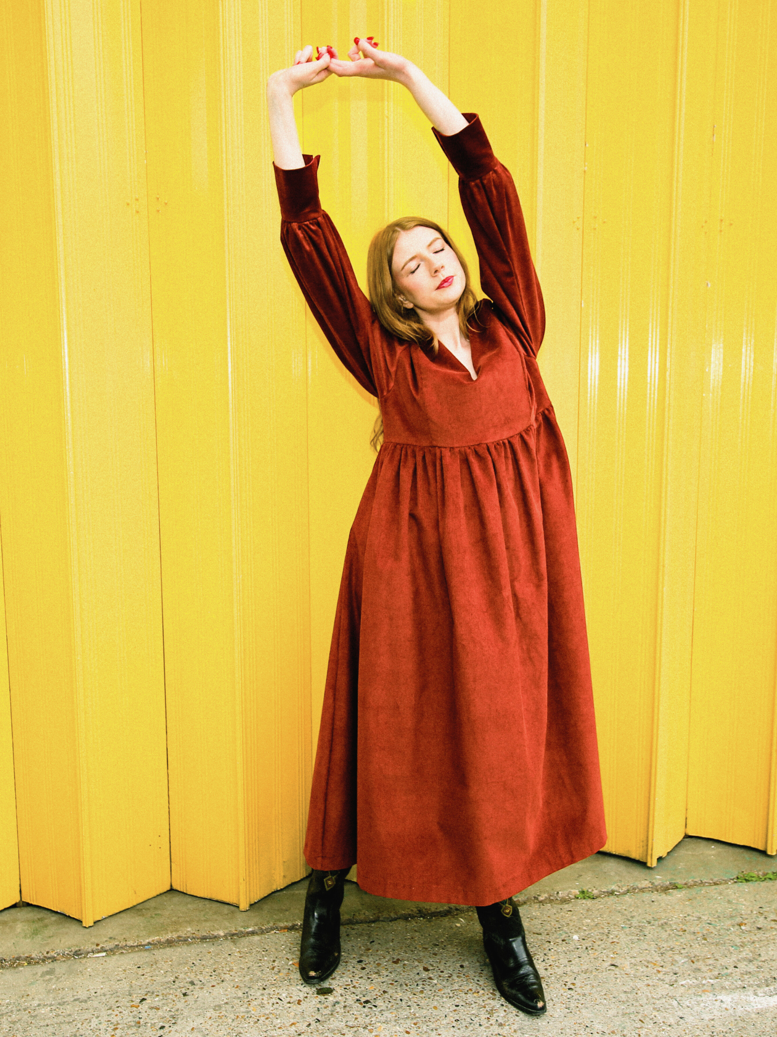 Woman in a rust red dress posing against a yellow wall