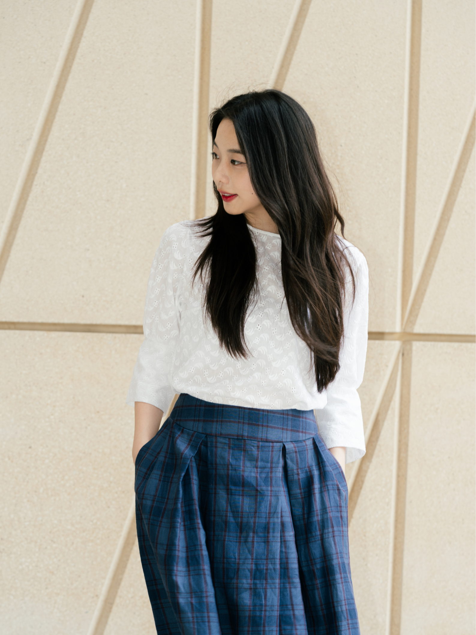 Woman wearing a white blouse and blue plaid pants against a beige wall.