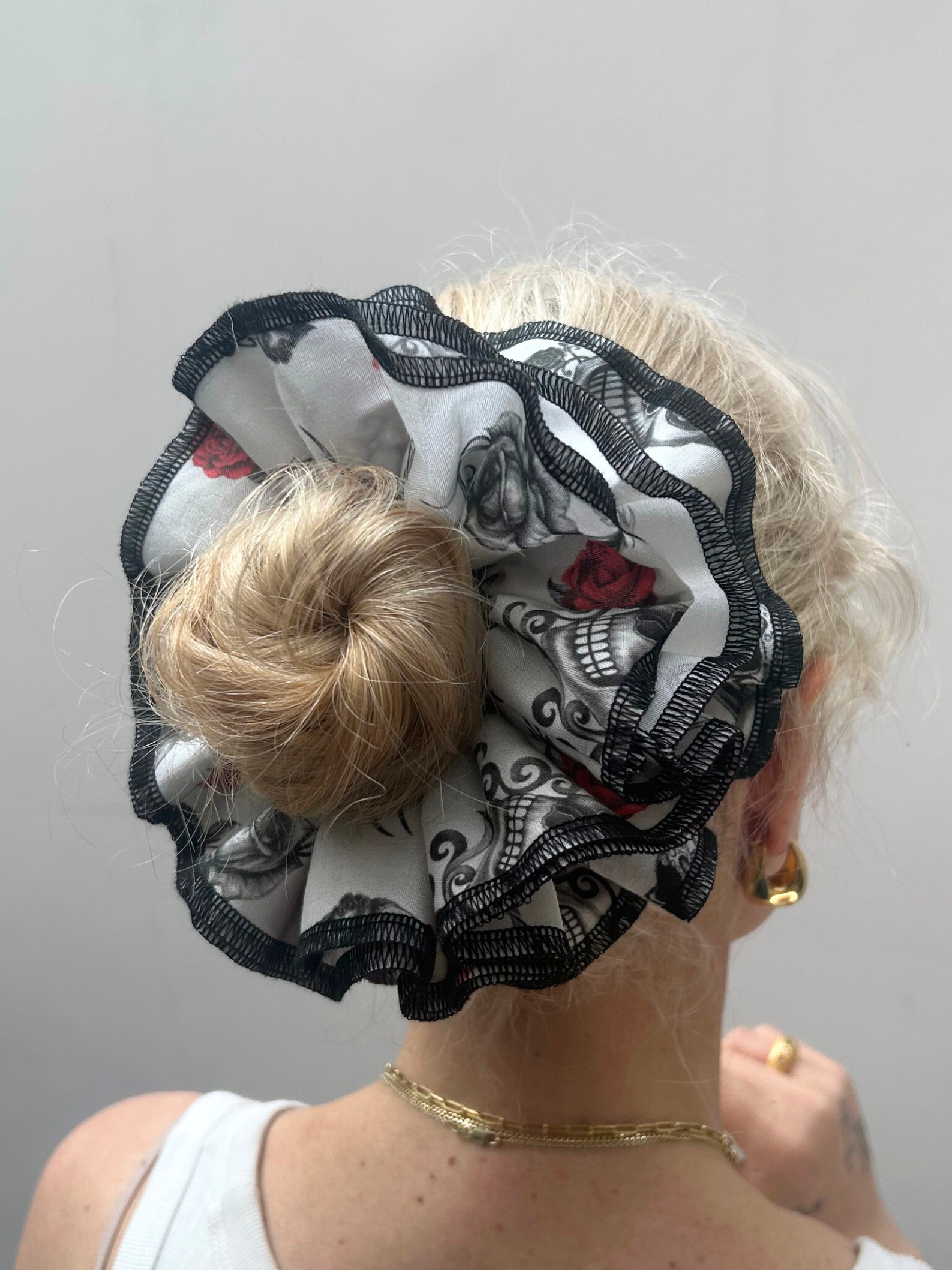 Person wearing a decorative hair scrunchie with skull and rose design on a plain background