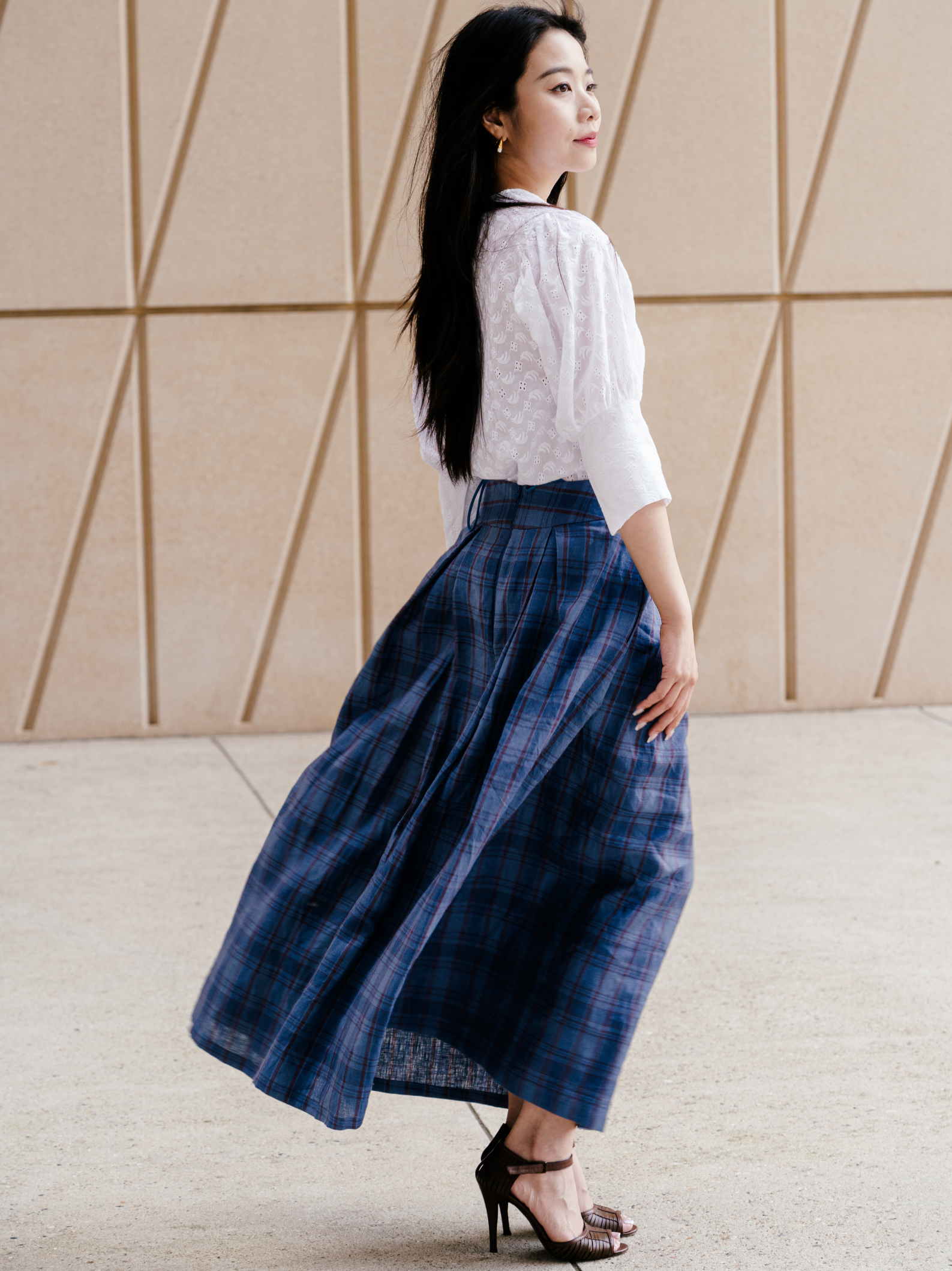 Woman wearing a white blouse and blue plaid skirt against a geometric wall.