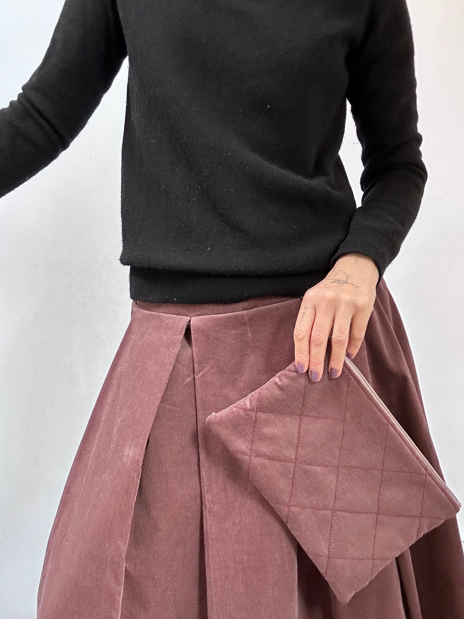 Person wearing a black sweater and pink pleated skirt on a white background
