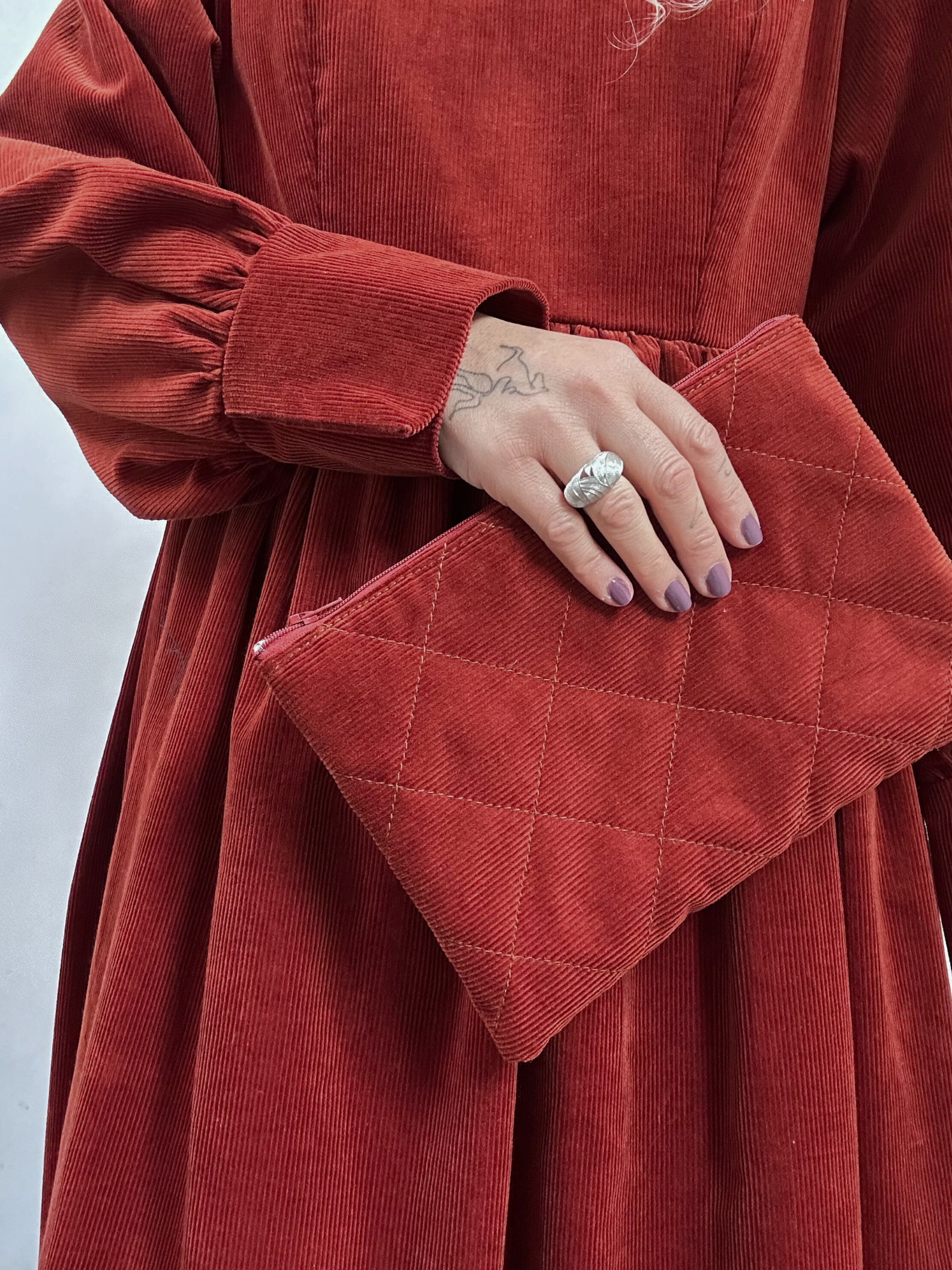 Red quilted clutch held by a person wearing a red corduroy dress against a white background