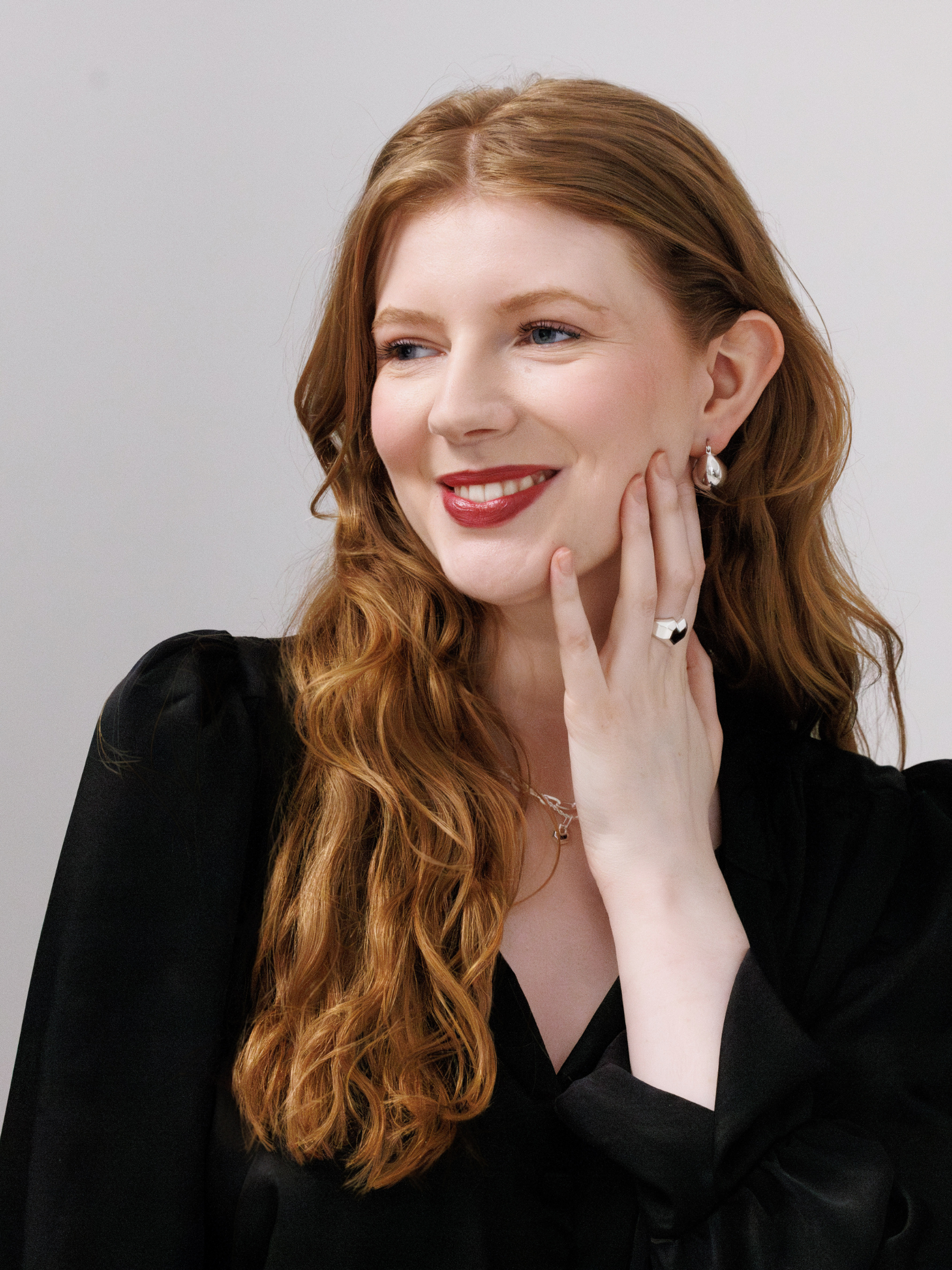 Woman with long red hair wearing a black outfit against a plain background