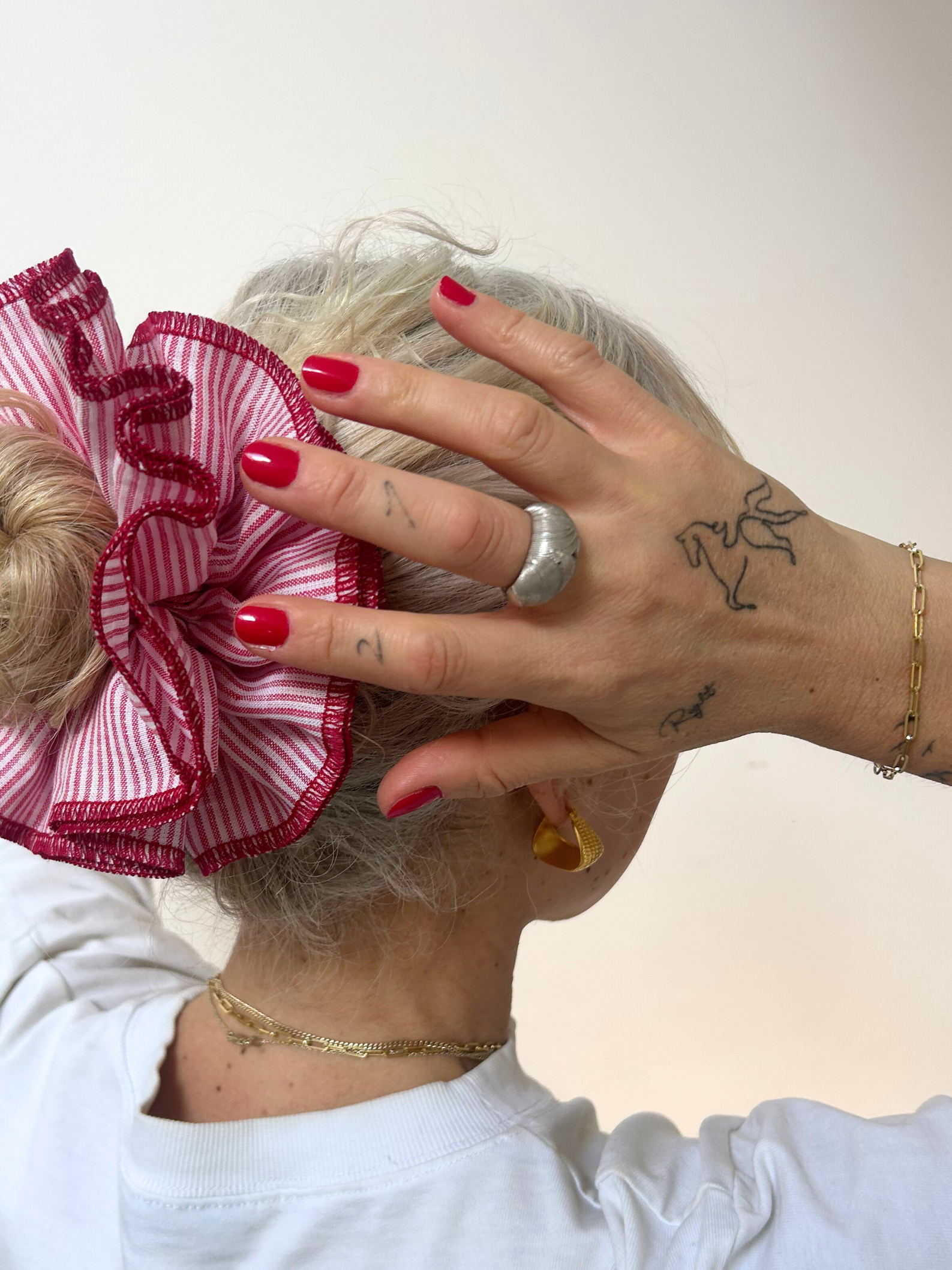 Person with a large red hair bow and red nail polish adjusting their hair against a white background