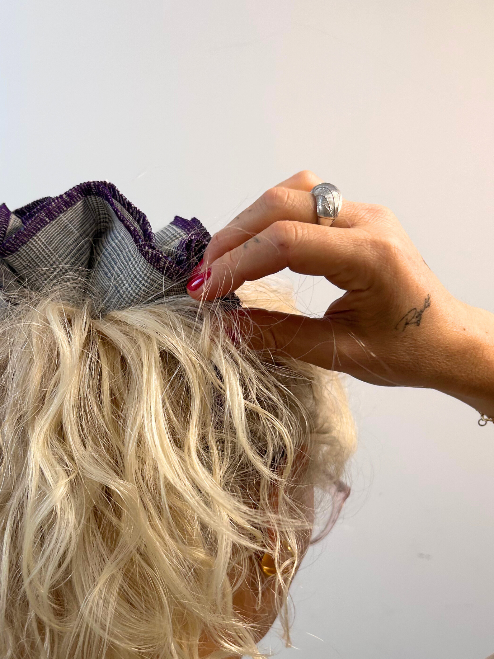 Person adjusting a grey hair scrunchie wearing a silver ring against a plain background