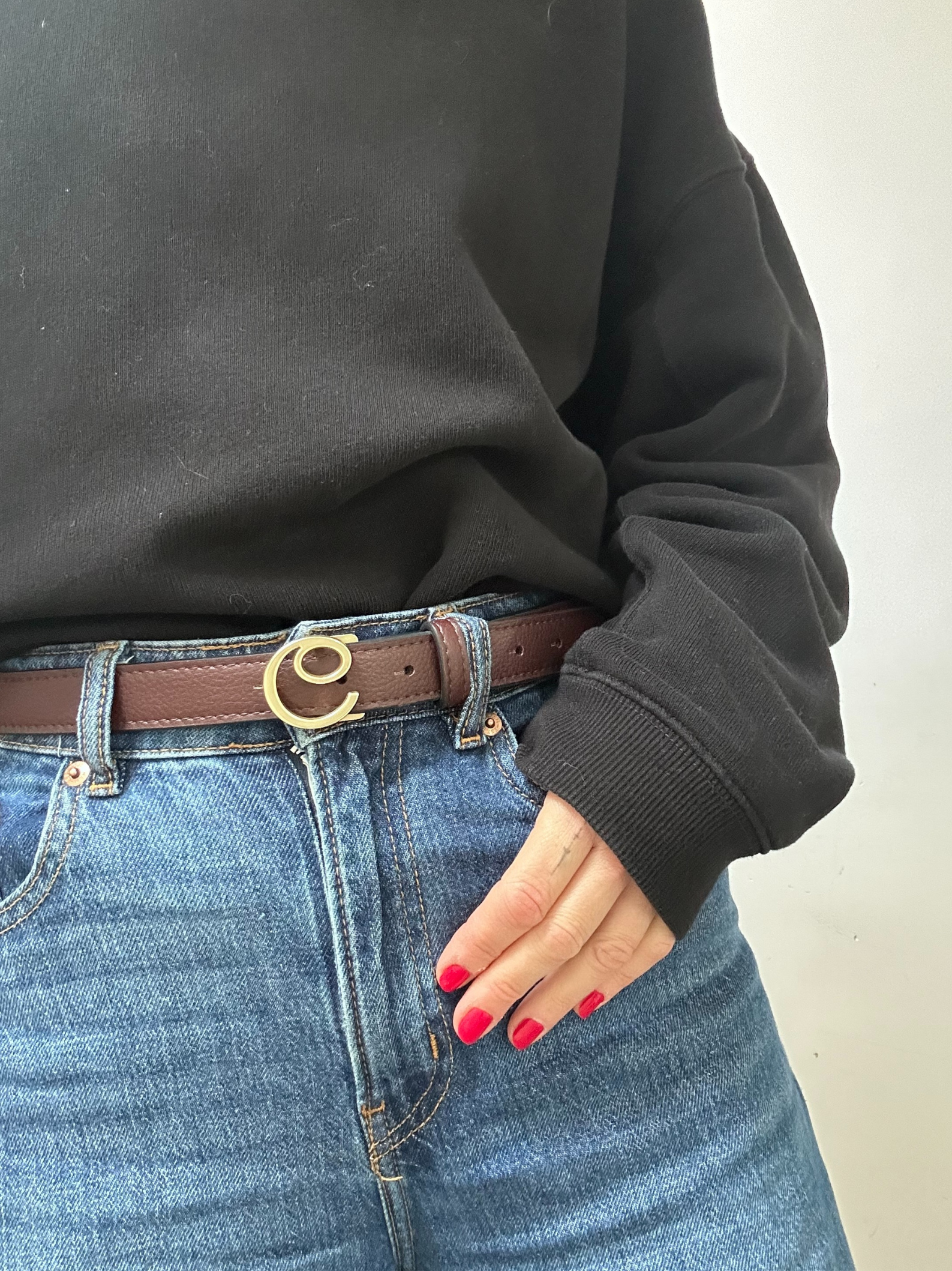 Person wearing a black sweatshirt and blue jeans with a brown belt featuring a gold buckle.