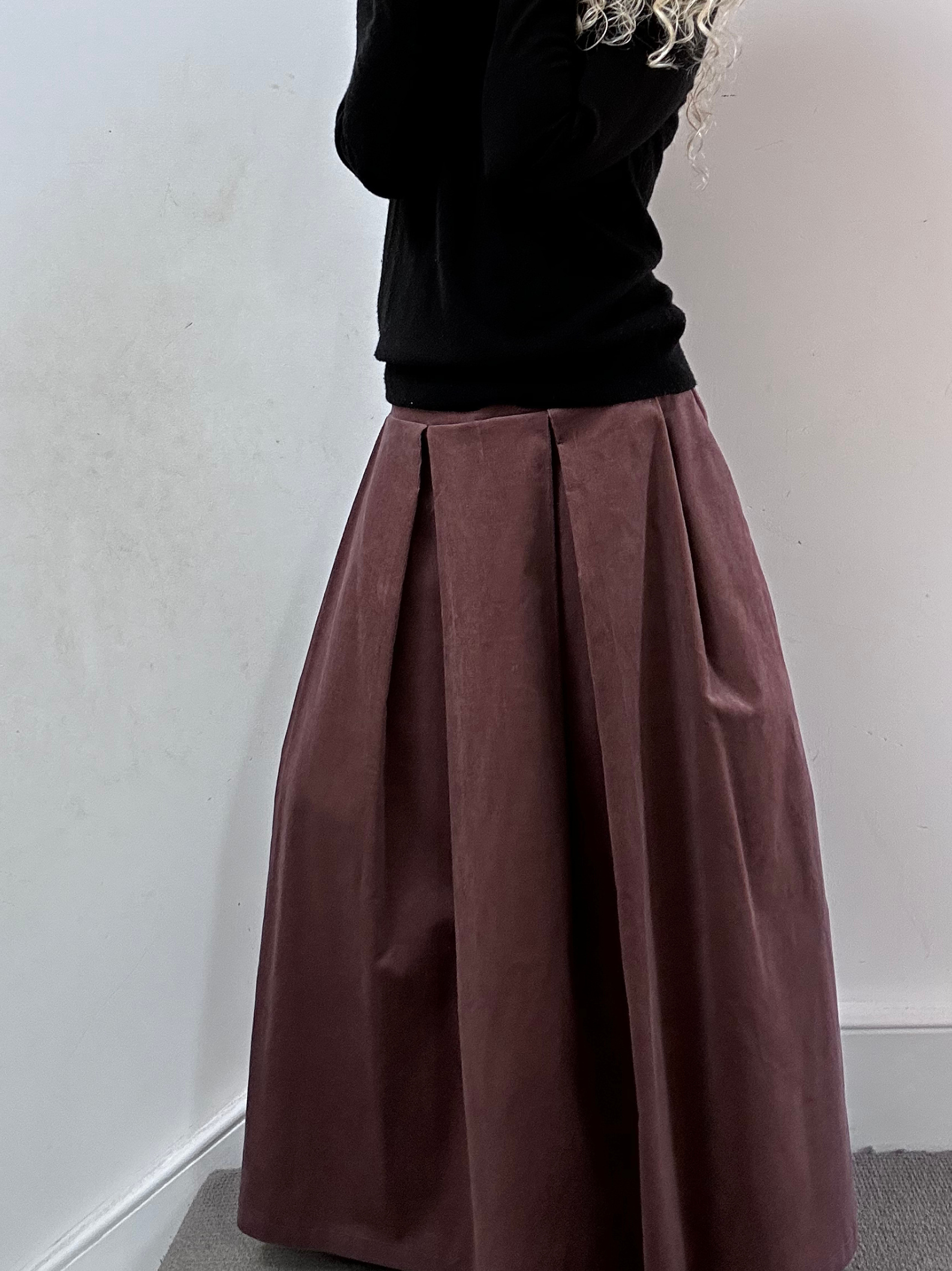 Person wearing a black top and print pleated skirt against a white wall.