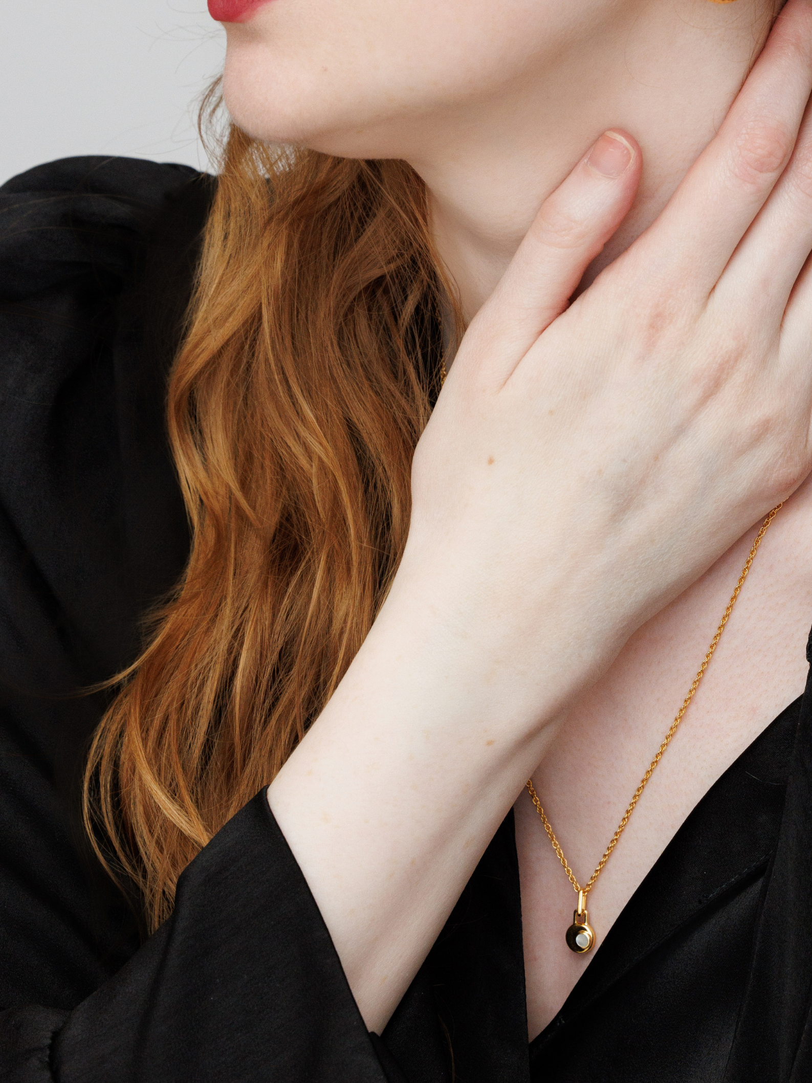 Woman wearing a gold necklace with a black pendant, touching her neck.