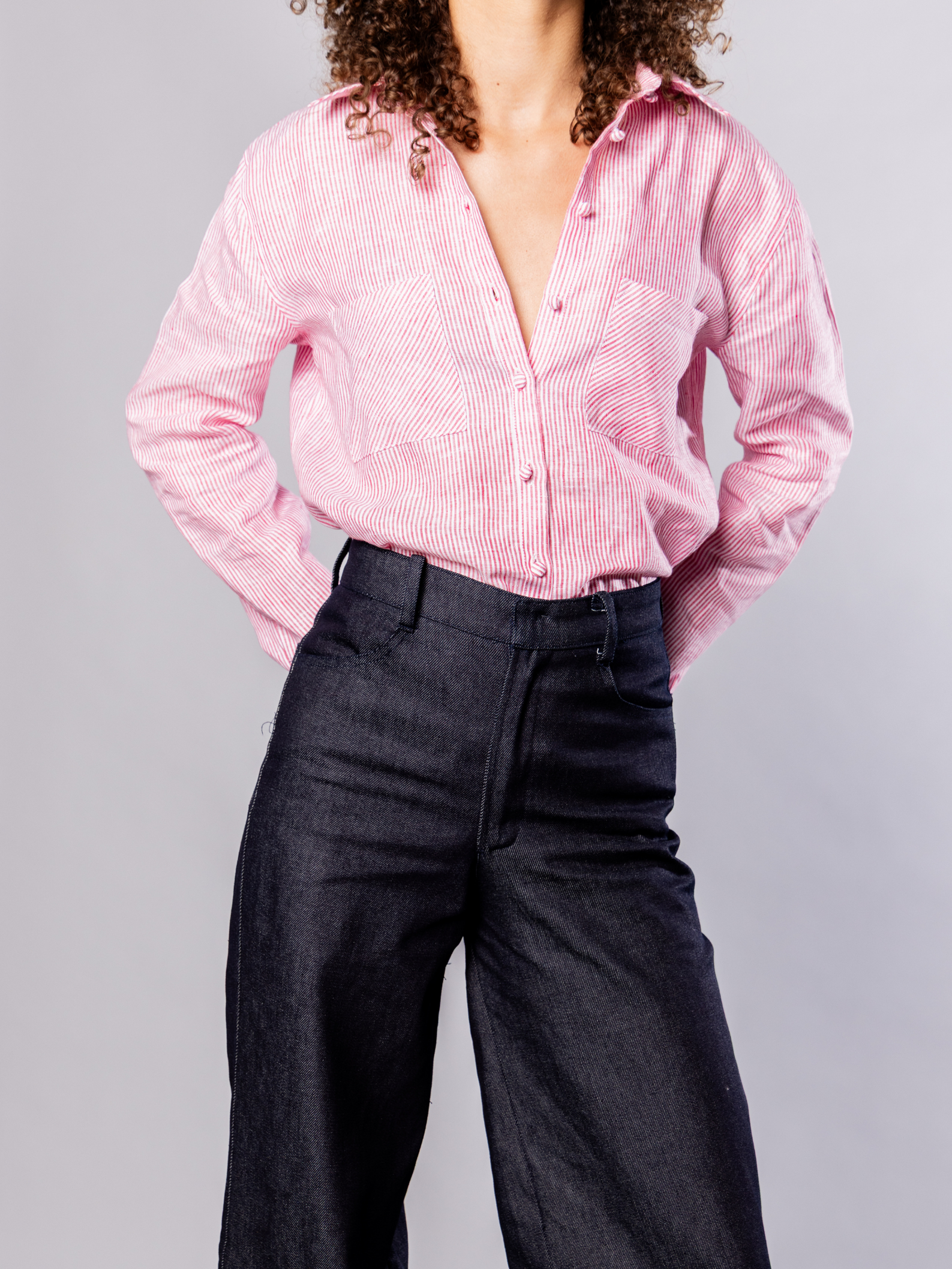 Person wearing a red striped shirt and dark navy denim pants on a grey background