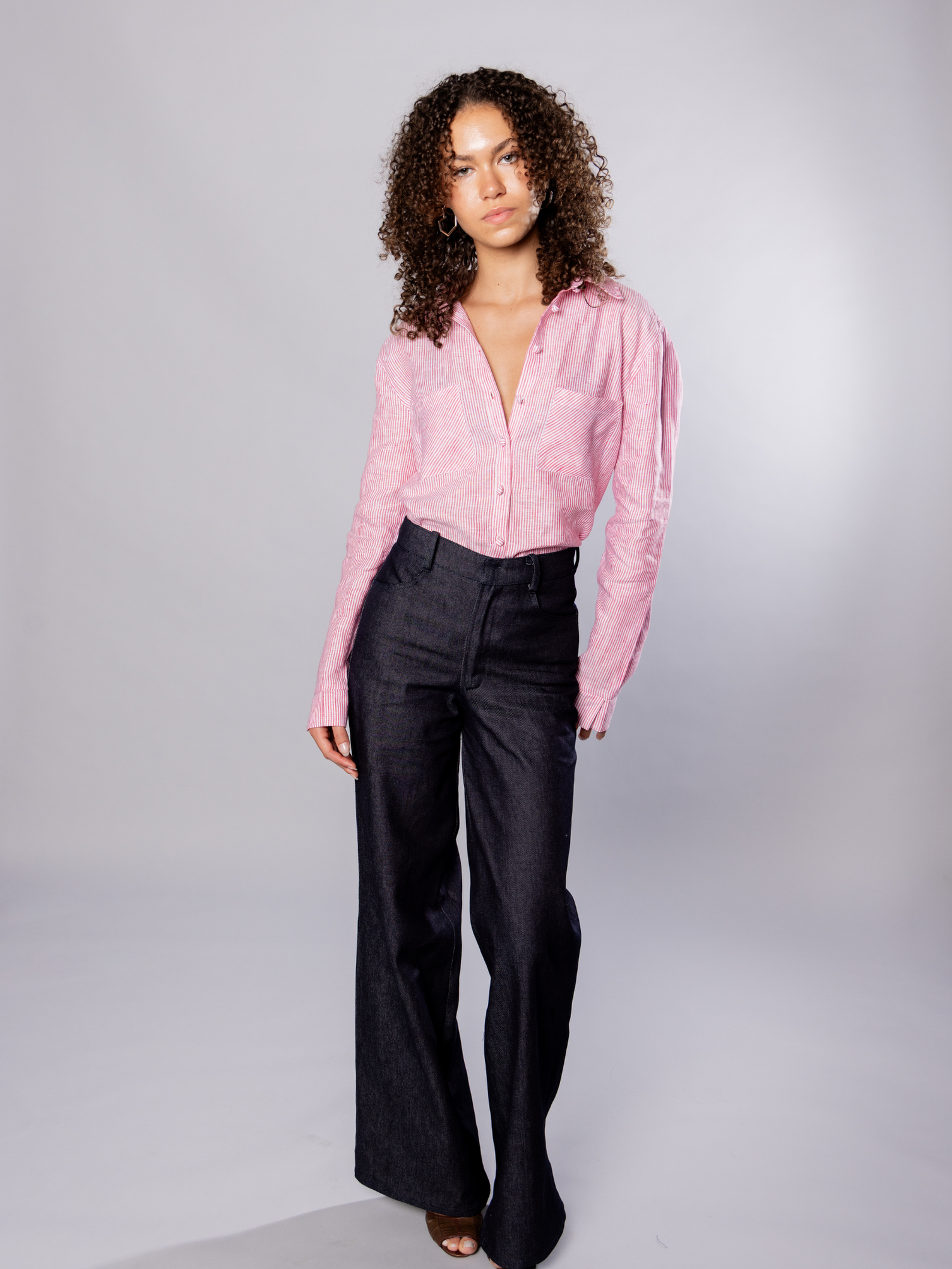 Woman wearing a red stripe blouse and dark navy denim pants against a plain background
