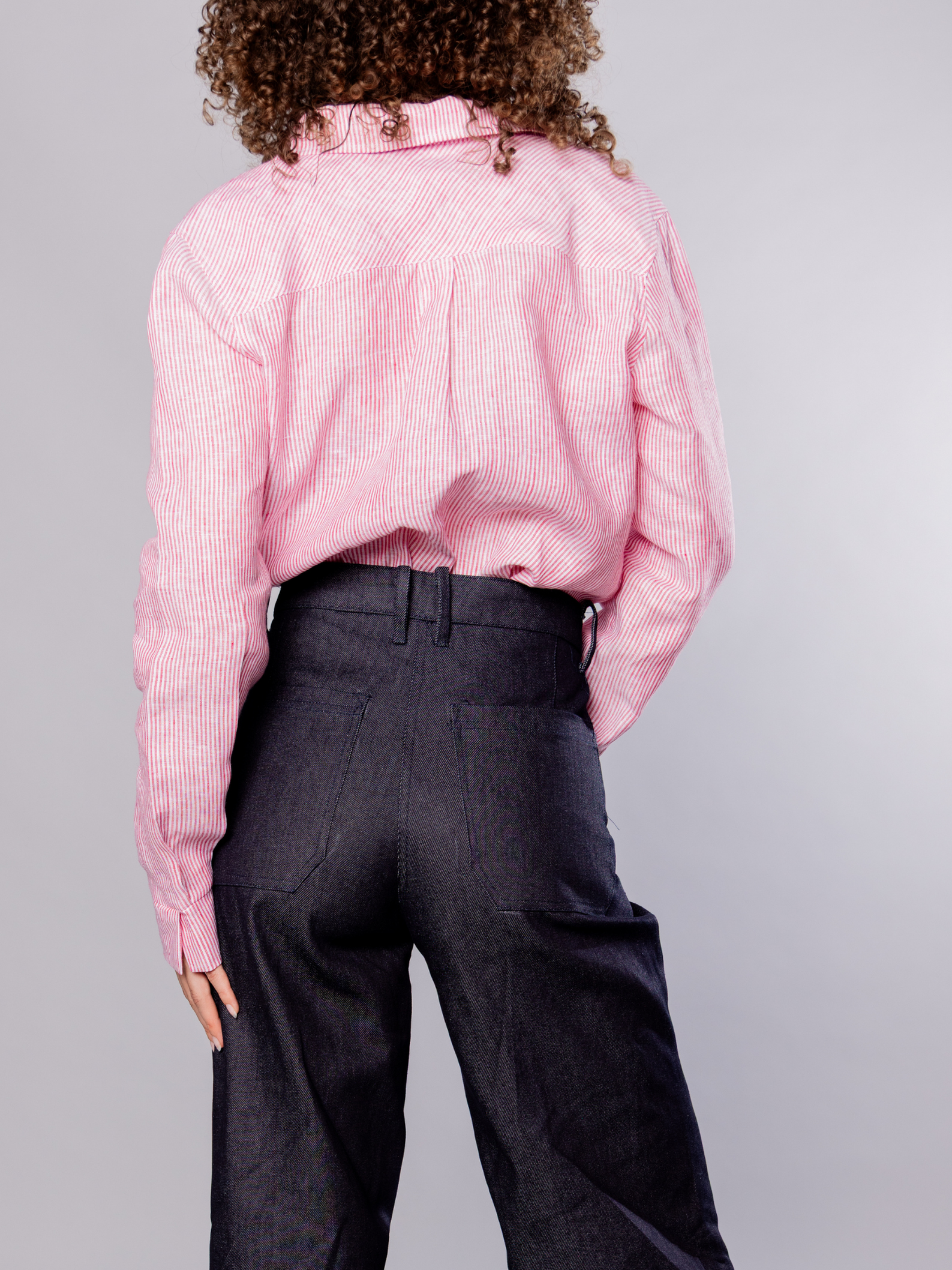 Person wearing a red stripe shirt and dark navy pants on a grey background