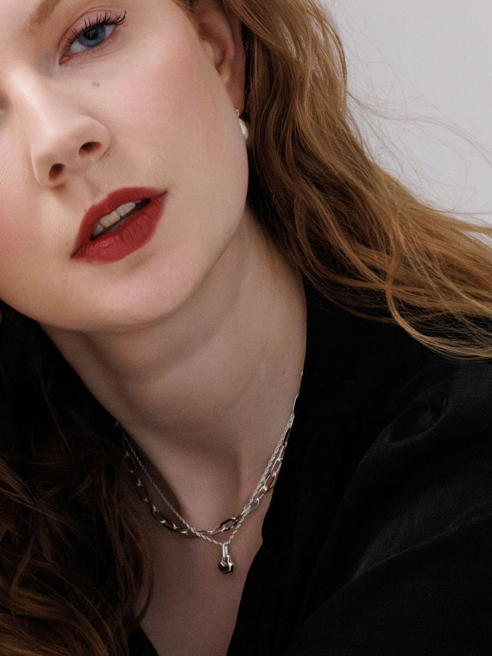 Close-up of a person wearing a silver necklace with a black background