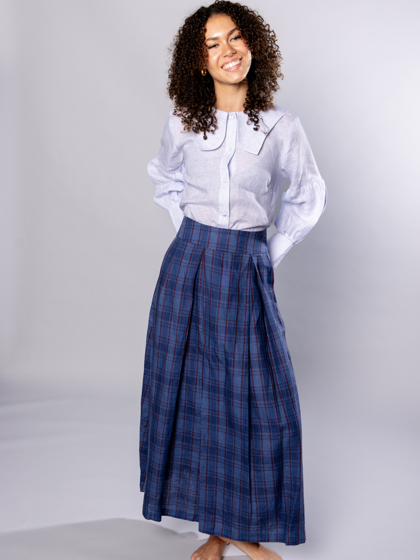 Woman wearing a white and light blue stripe blouse and navy blue plaid skirt on a grey background