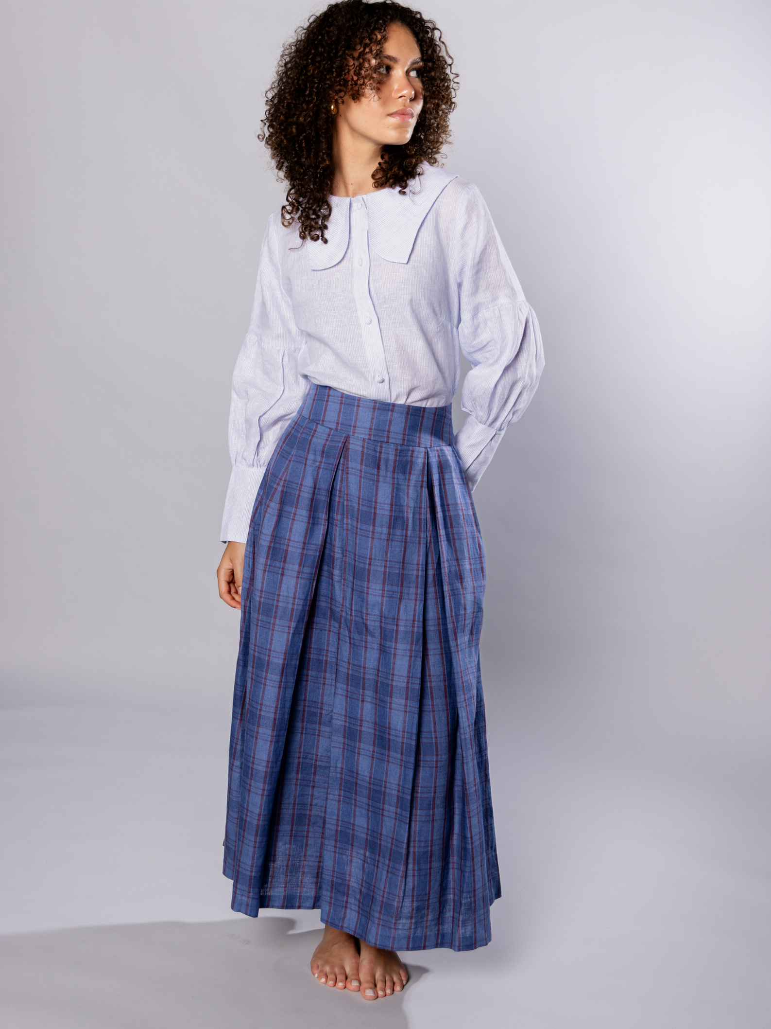 Woman wearing a white and light blue shirt and navy blue plaid skirt on a plain background