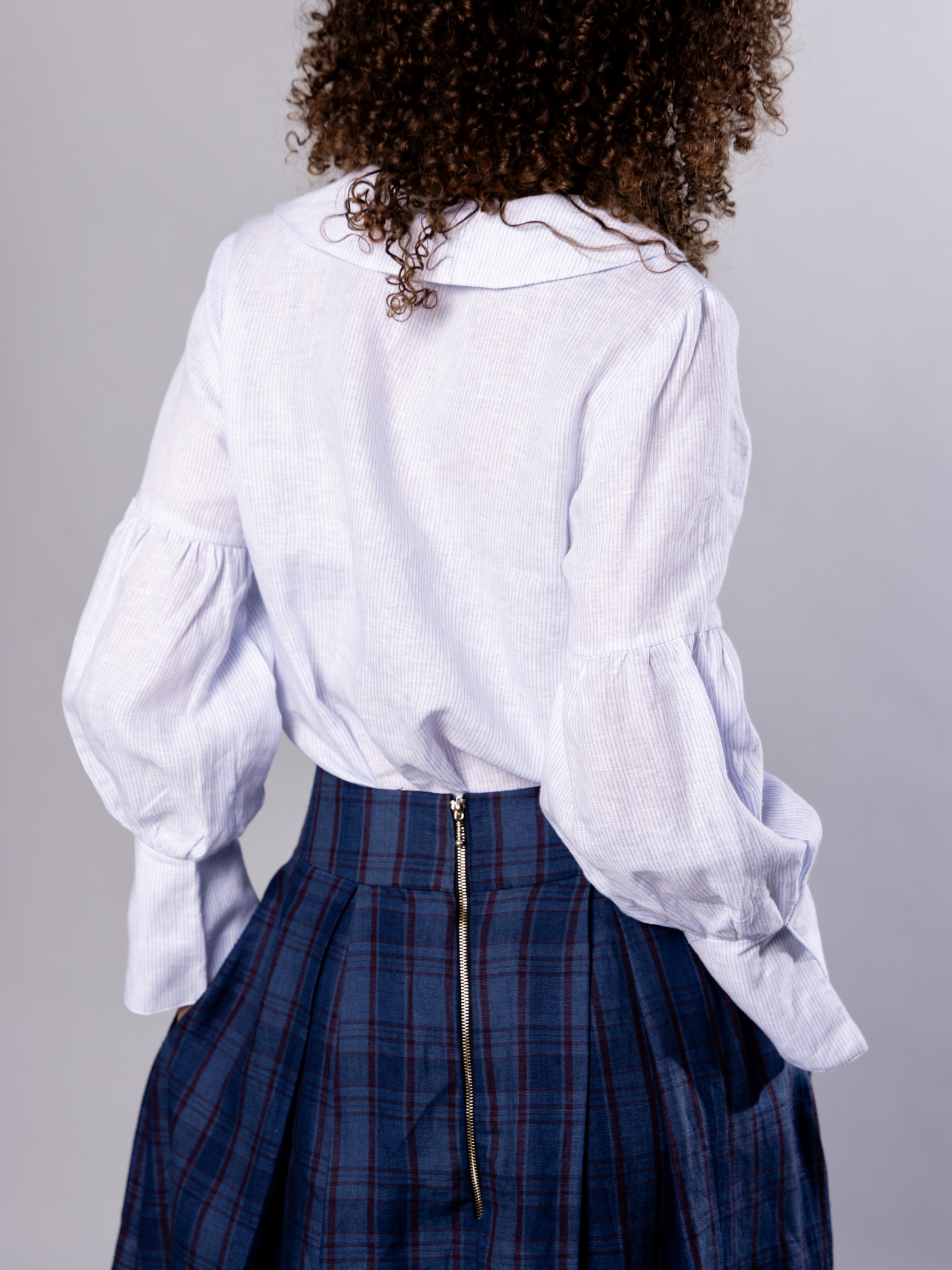 Person wearing a white ands blue stripe blouse and navy blue plaid skirt on a grey background