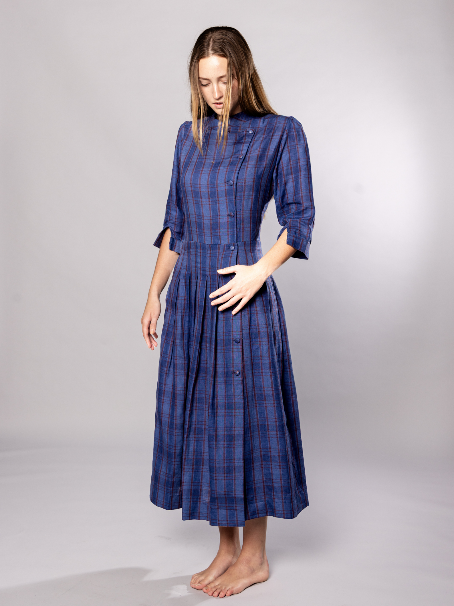 Woman wearing a navy blue plaid dress with side buttons on a grey background