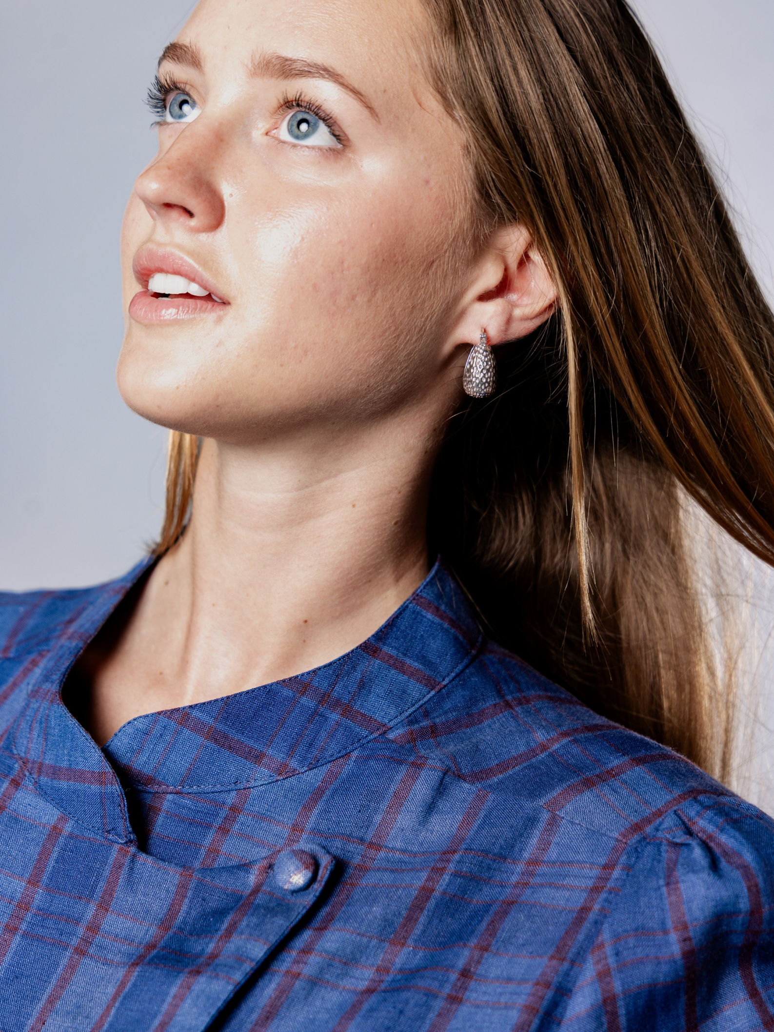 Woman wearing a navy blue plaid dress with silver hoop earrings with a neutral background