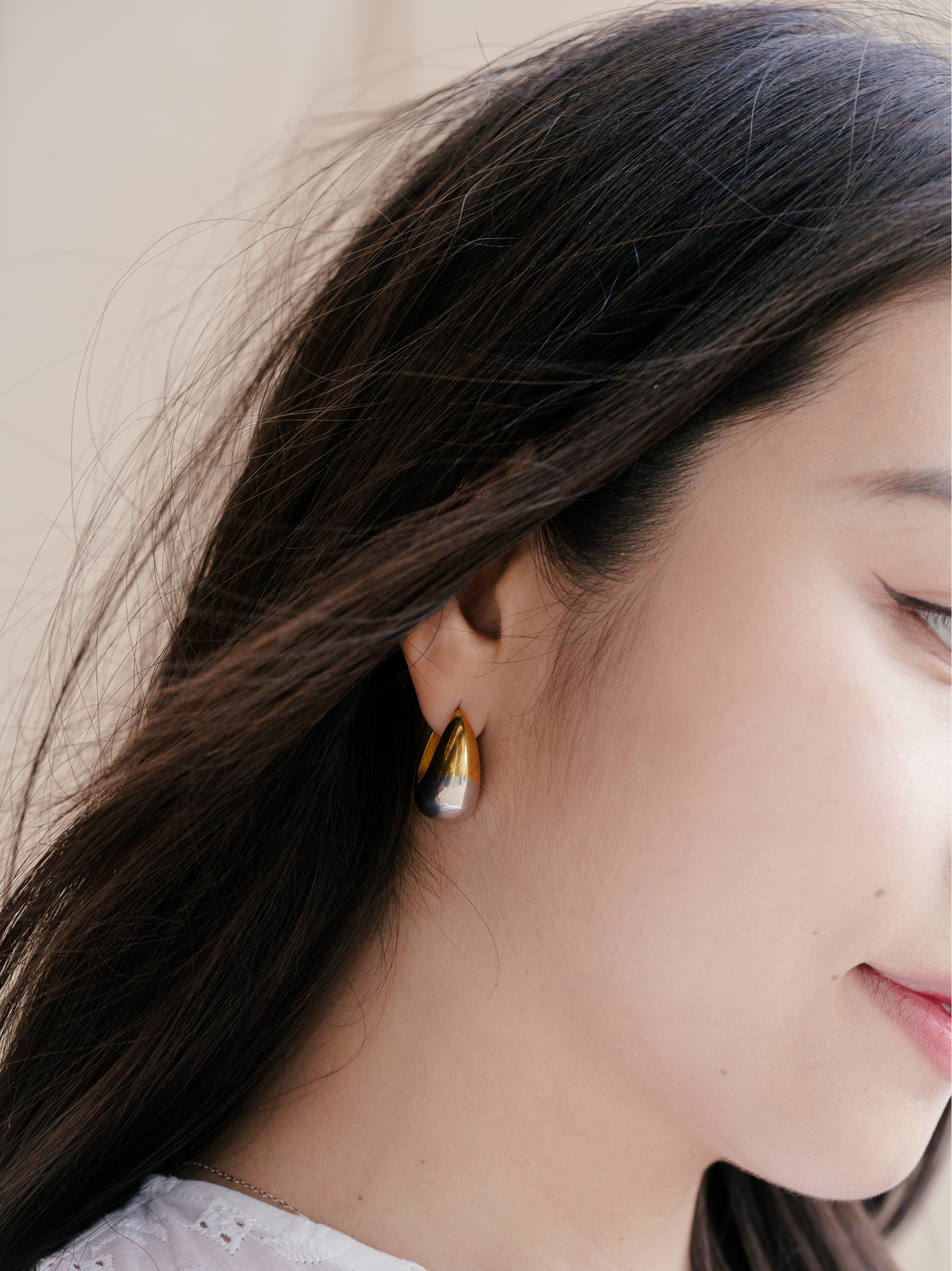 Close-up of a person wearing a gold and silver earring with a neutral background