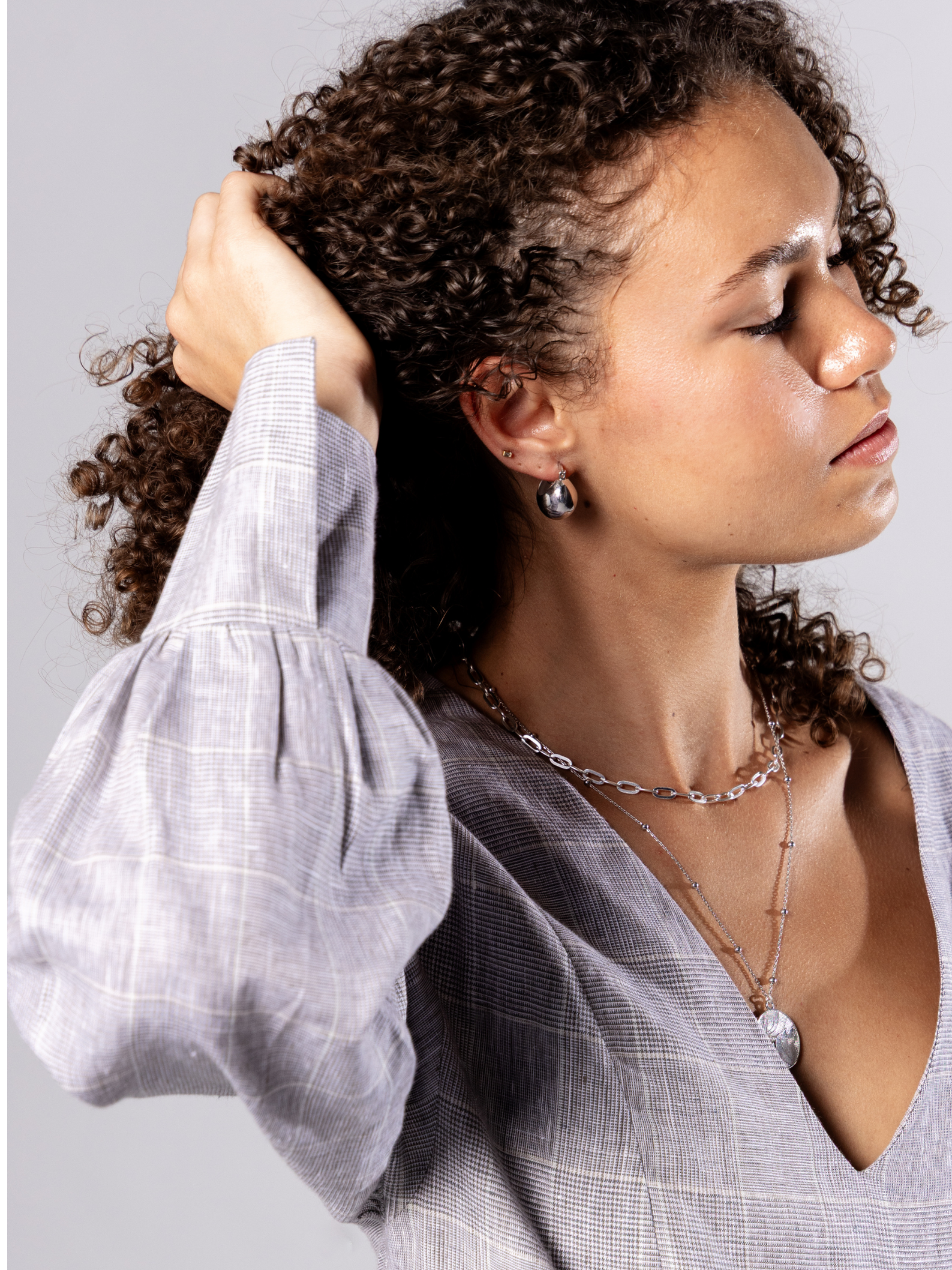 Woman wearing a light grey v neck dress with puffed sleeves and silver chain necklace against a plain background