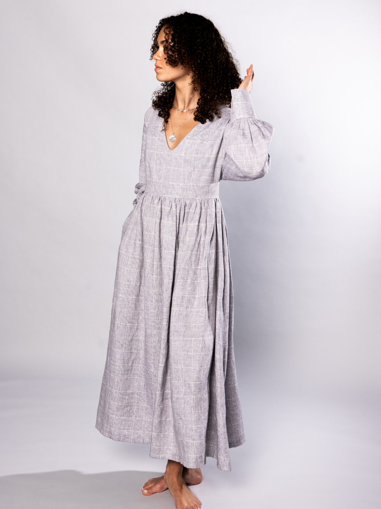 Woman wearing a long grey v neck dress against a white background