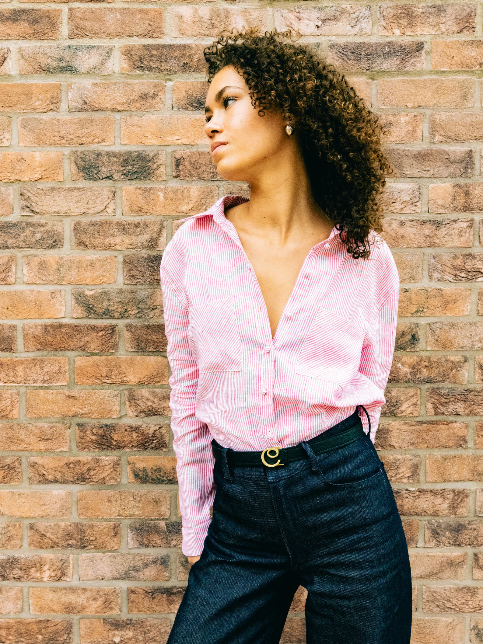 Woman wearing a red stripe shirt and dark navy denim pants against a brick wall
