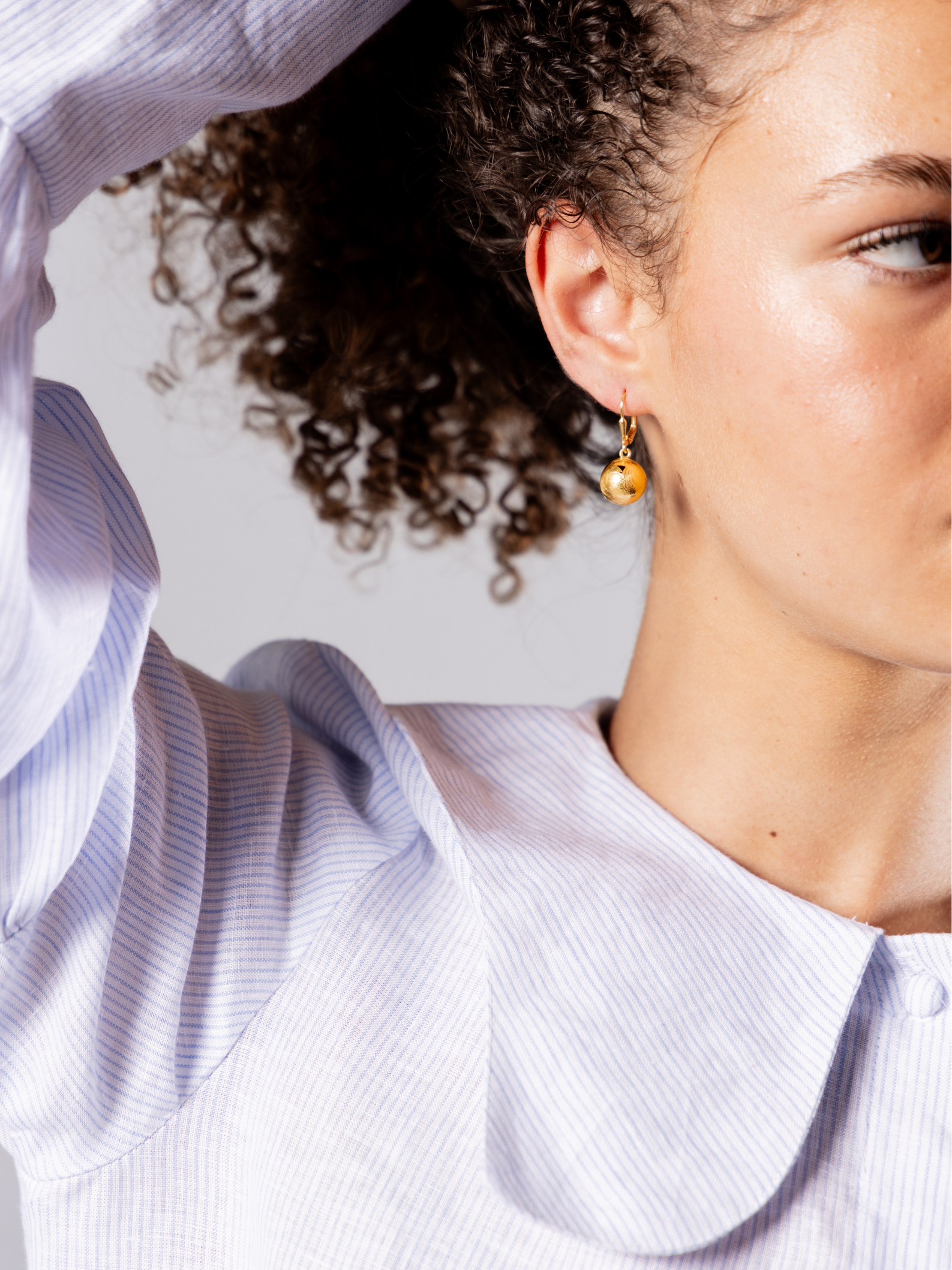 Close-up of a person wearing a light blue shirt with ruffled sleeves and gold drop ball earrings.