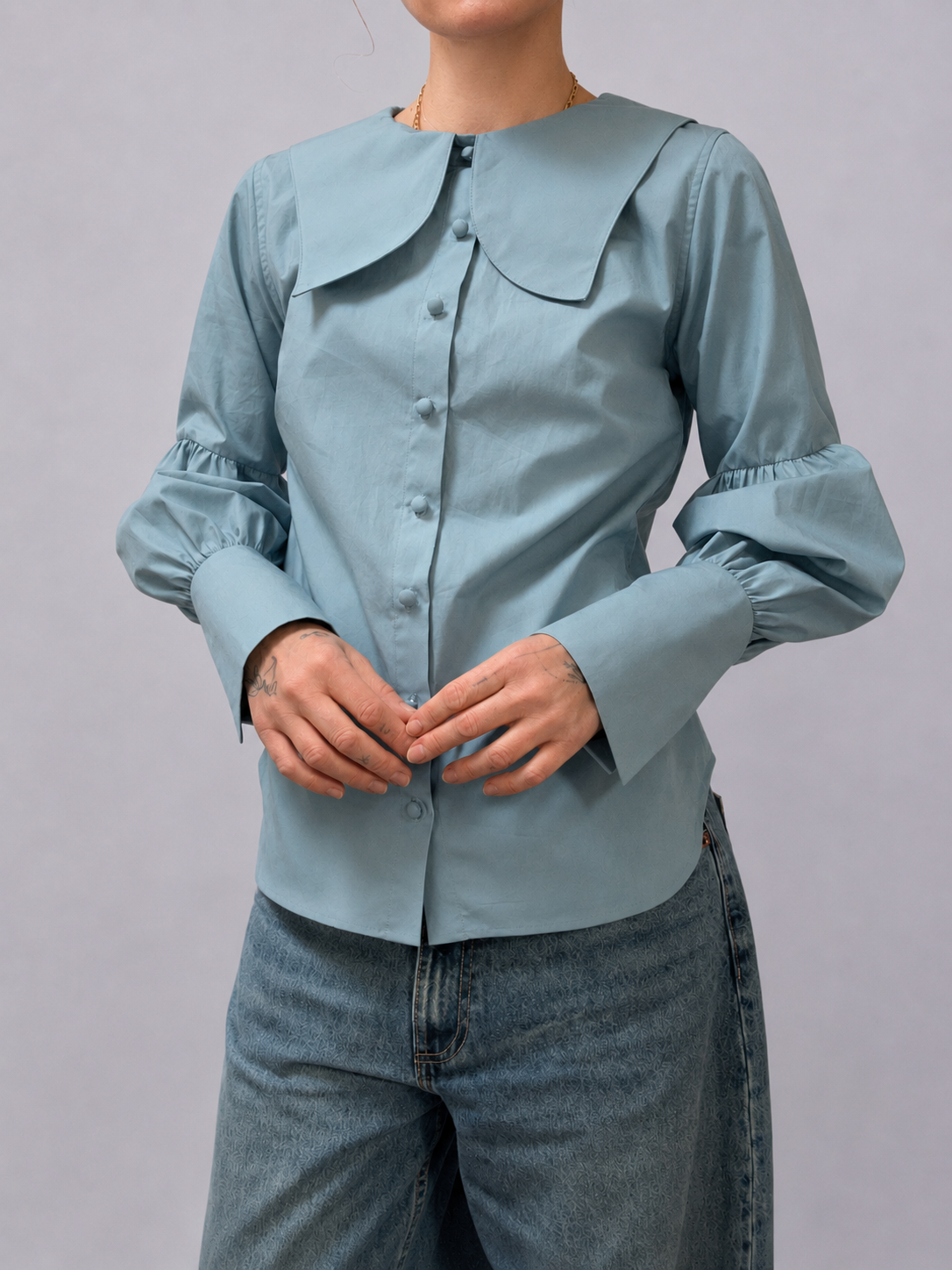 a woman wearing a blue blouse with buttons, puffy sleeves and a big collar