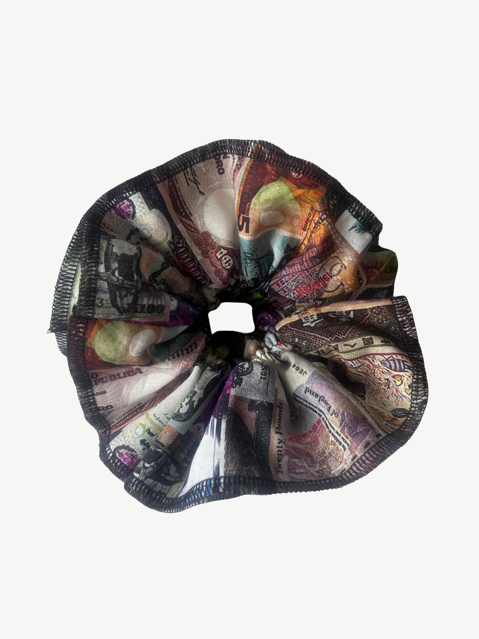 A fabric hair scrunchie featuring an all-over print of various banknotes and currency notes, with a dark navy blue stitched edge, shown against a plain light gray background.