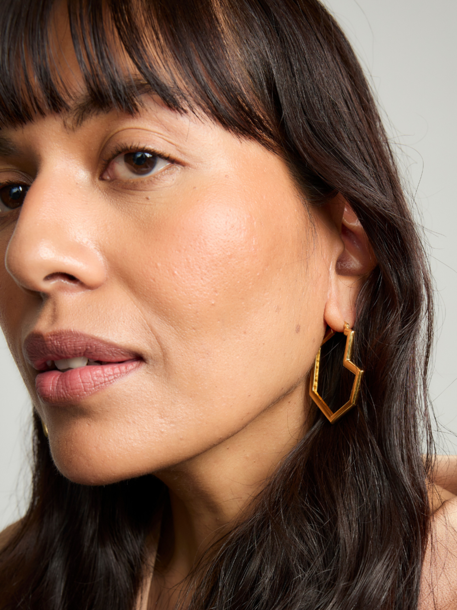 Close-up of a woman wearing gold hoop earrings with a neutral background