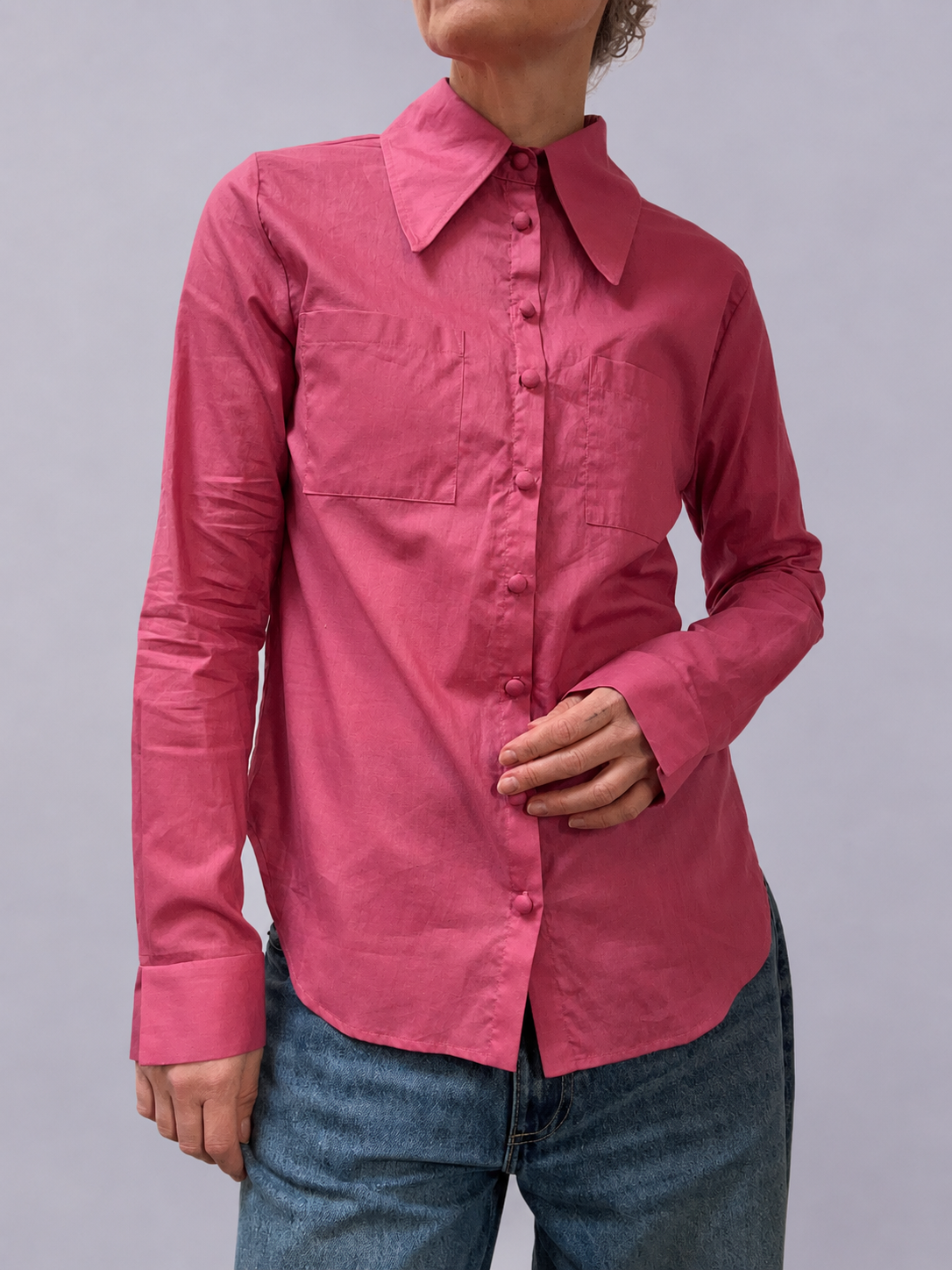 Person wearing a pink shirt with a collar against a gray background