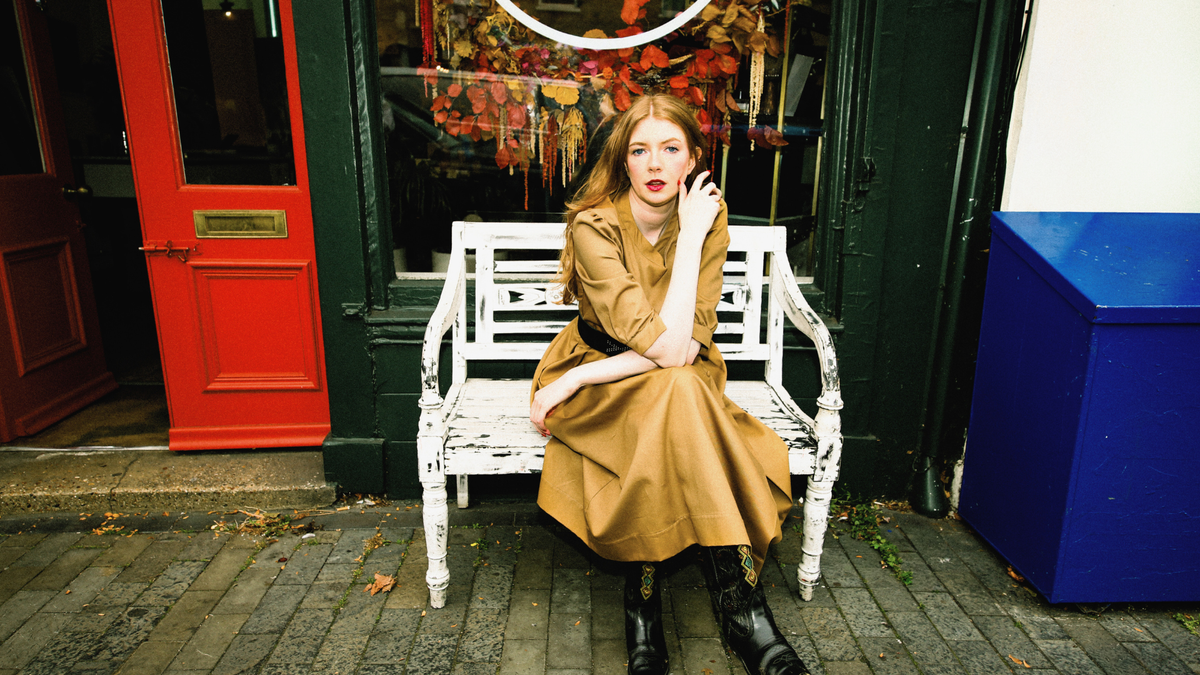 a woman wearing a brown dress is sitting on a bench outside a shop