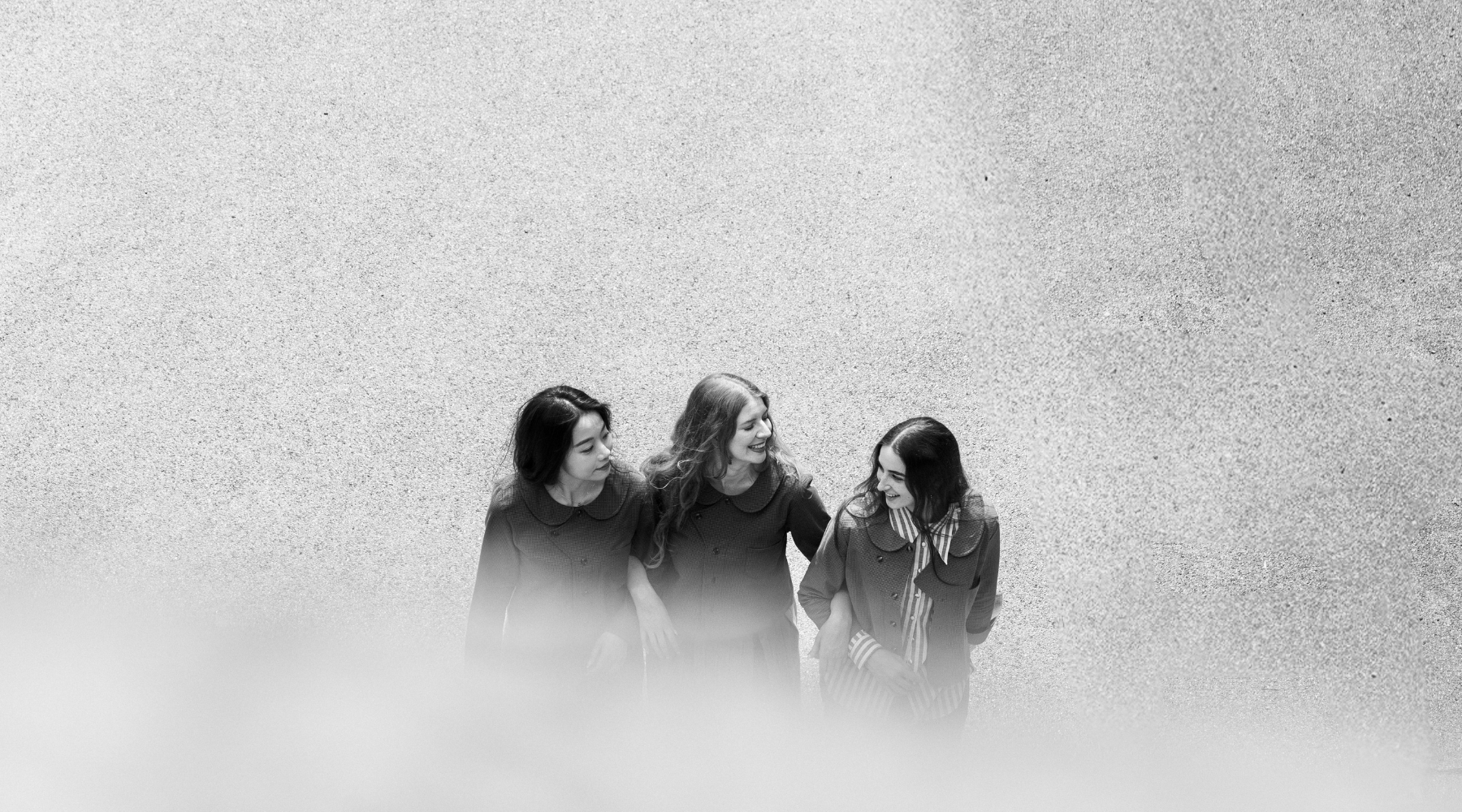 black and white image of three women walking alongside eachother laughing and holding hands