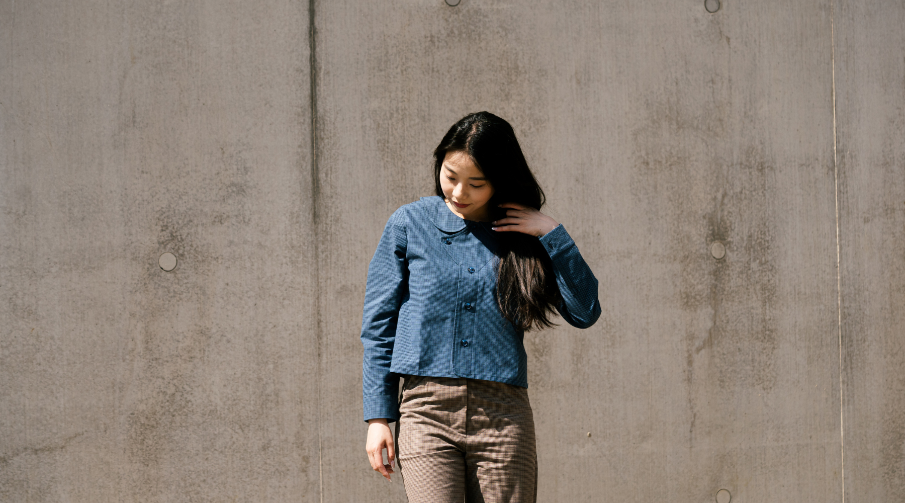 asian woman with long black hair, wearing a blue jacket standing in front of the concrete wall