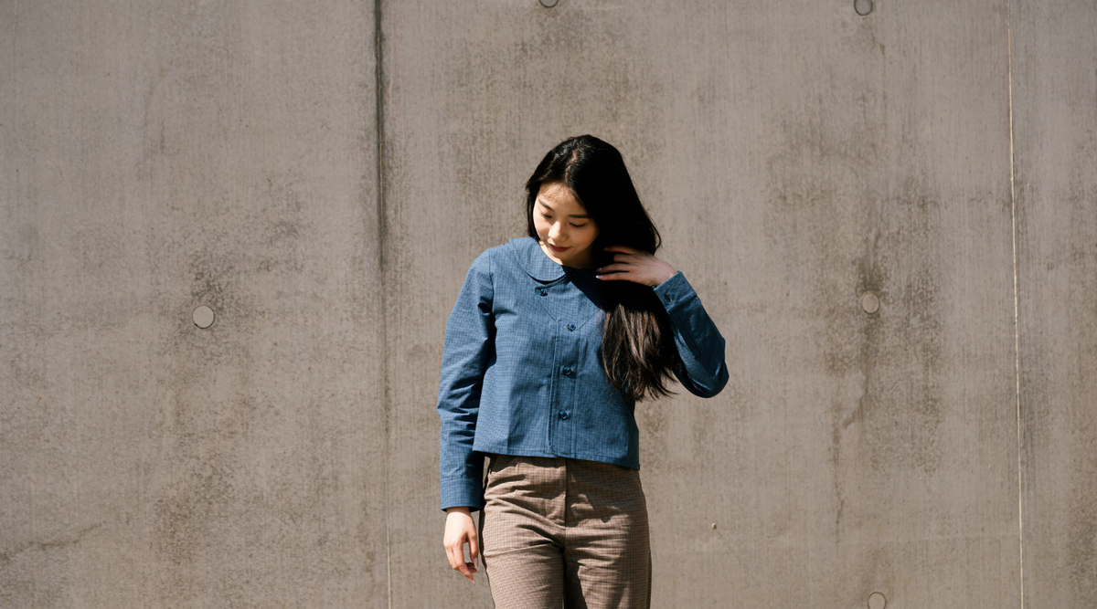 asian woman with long black hair, wearing a blue jacket standing in front of the concrete wall