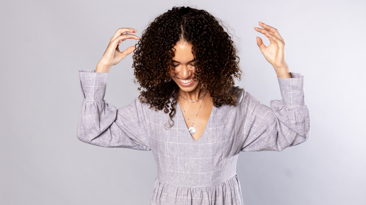 woman with a black curly hair wearing a grey dress is smiling