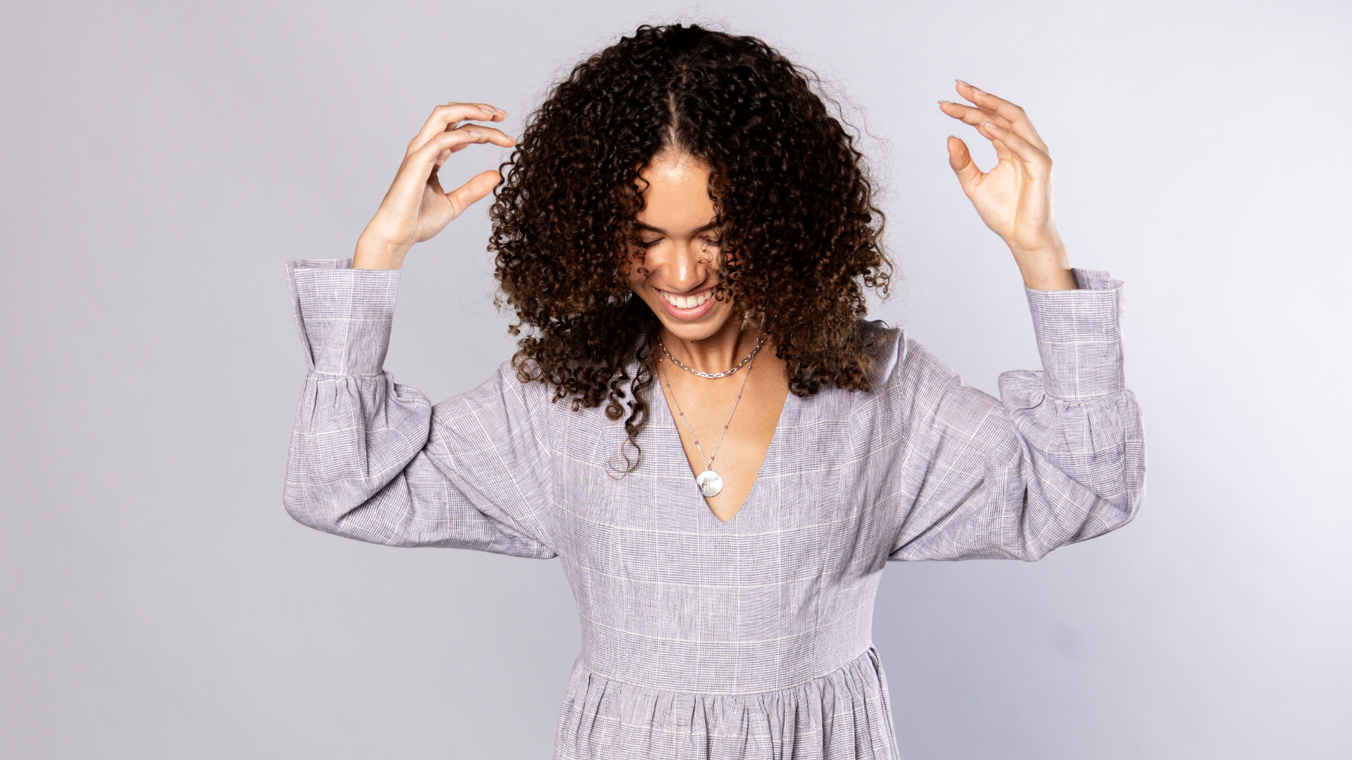 woman with a black curly hair wearing a grey dress is smiling