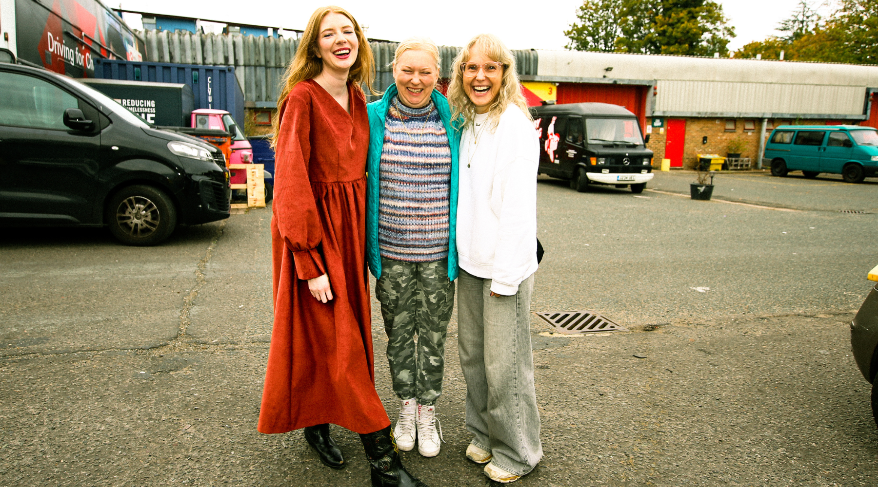 3 blonde women smiling and hugging in an industrial carpark