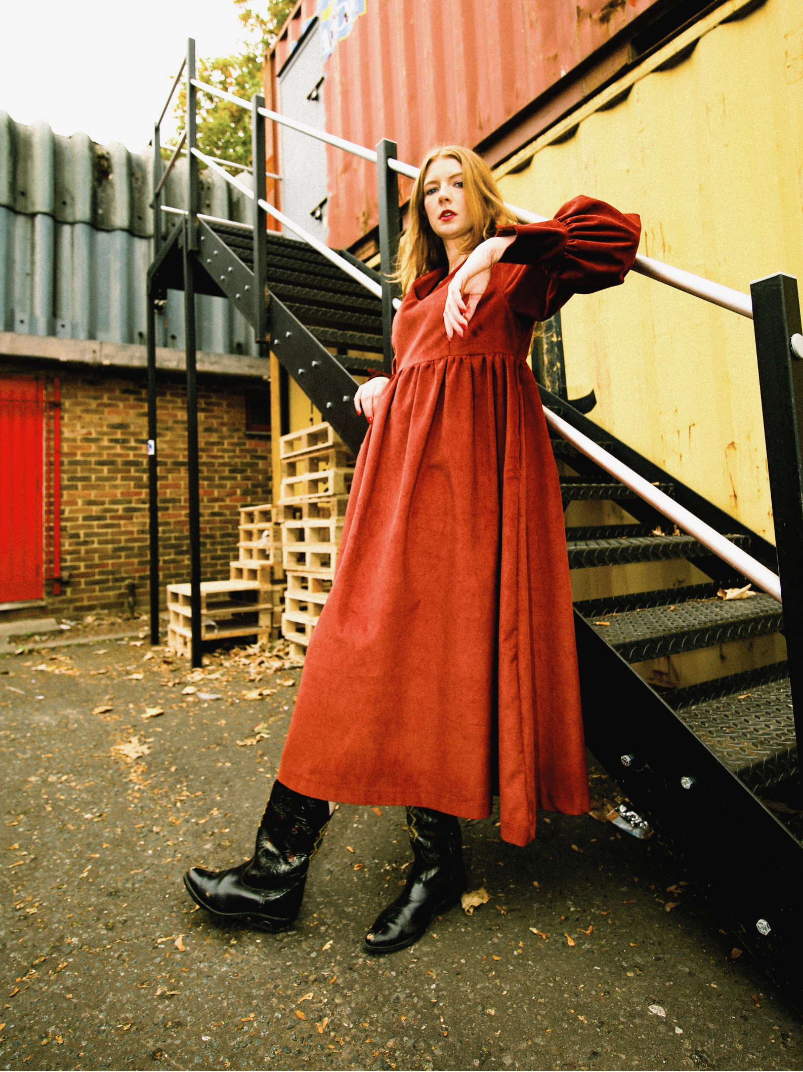 Woman in a red rust dress standing on a staircase with industrial background
