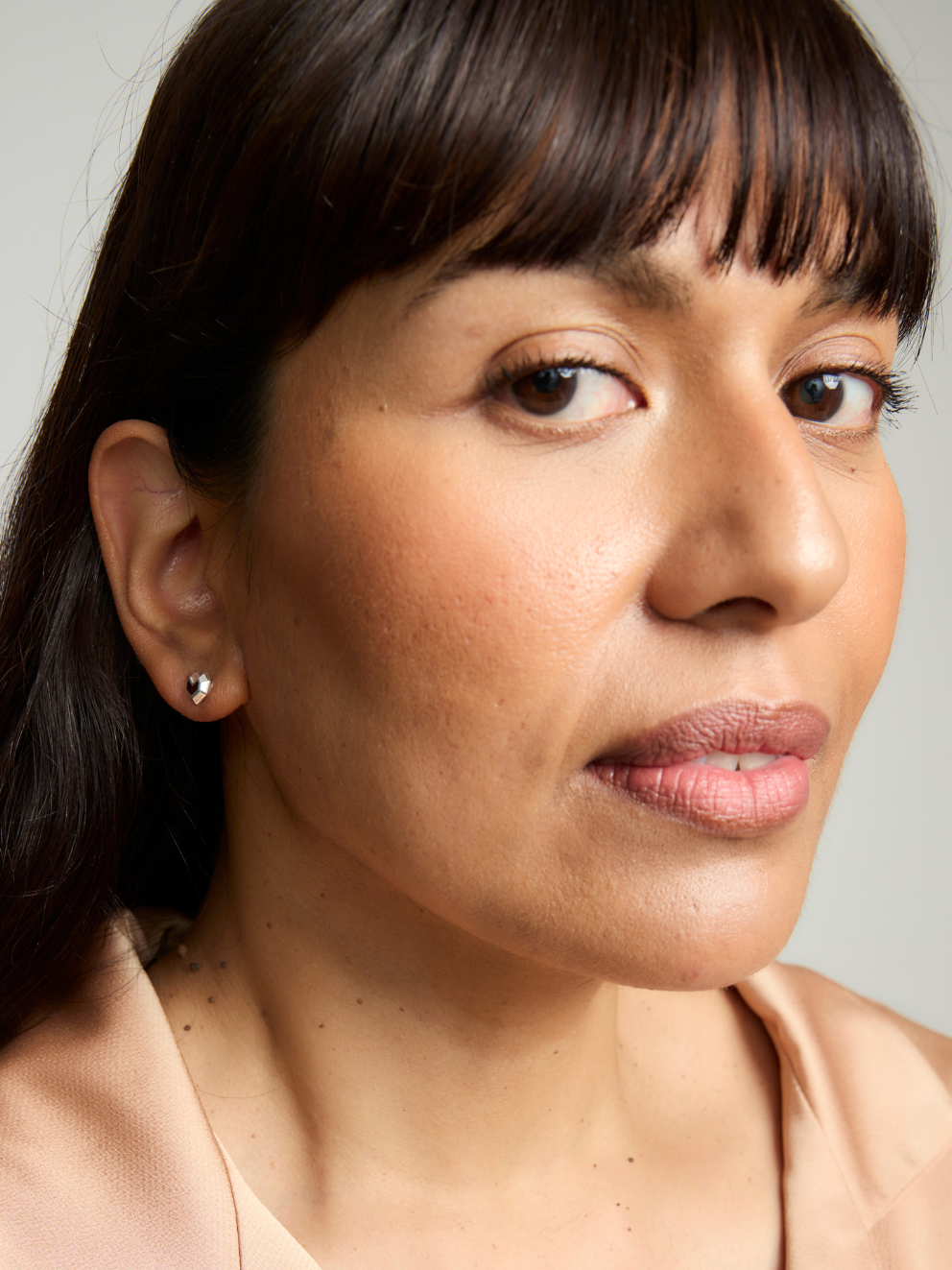 Close-up of a woman with dark hair and silver earrings against a neutral background