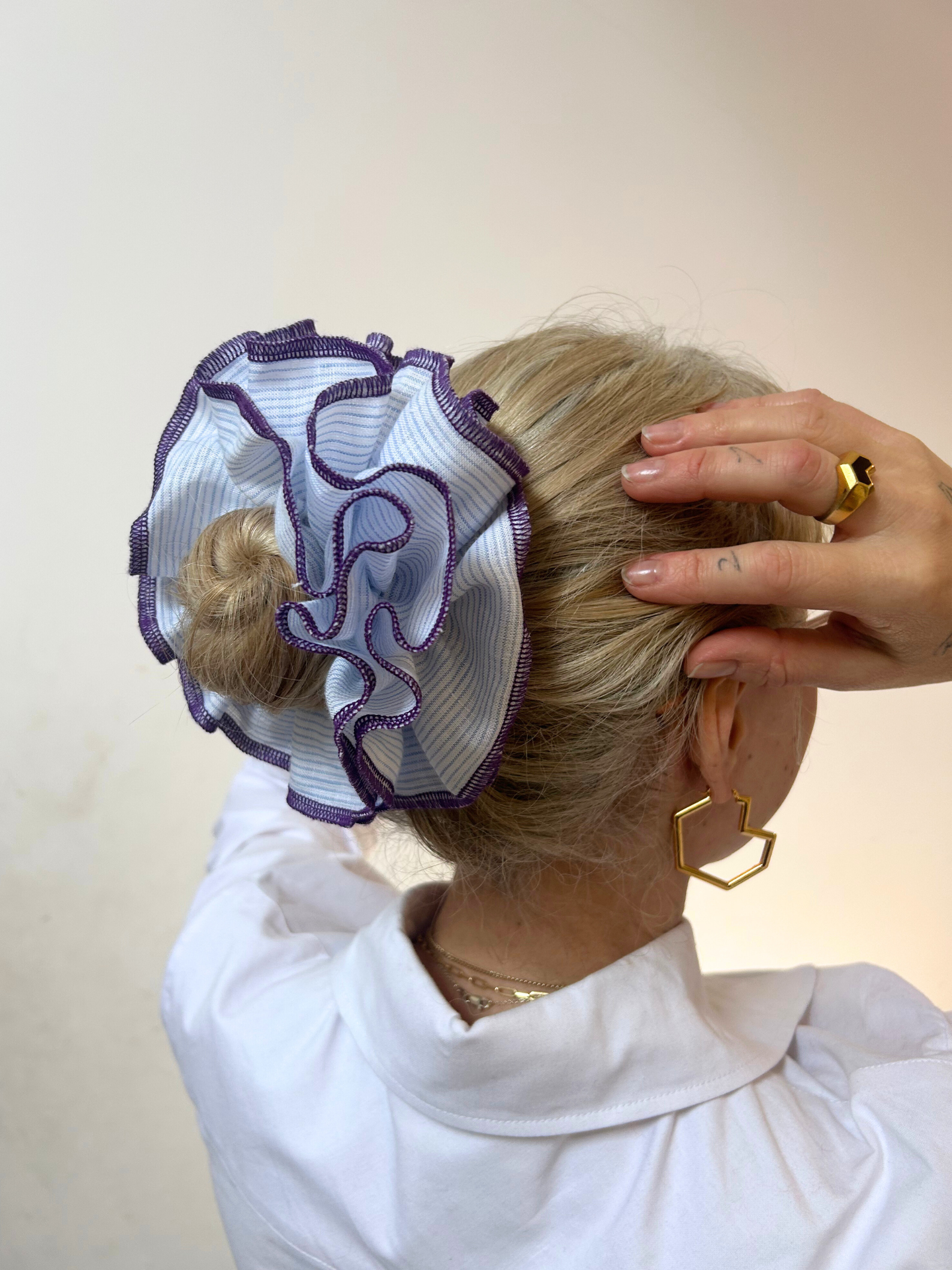 Person wearing a decorative hair scrunchie with intricate design on a plain background