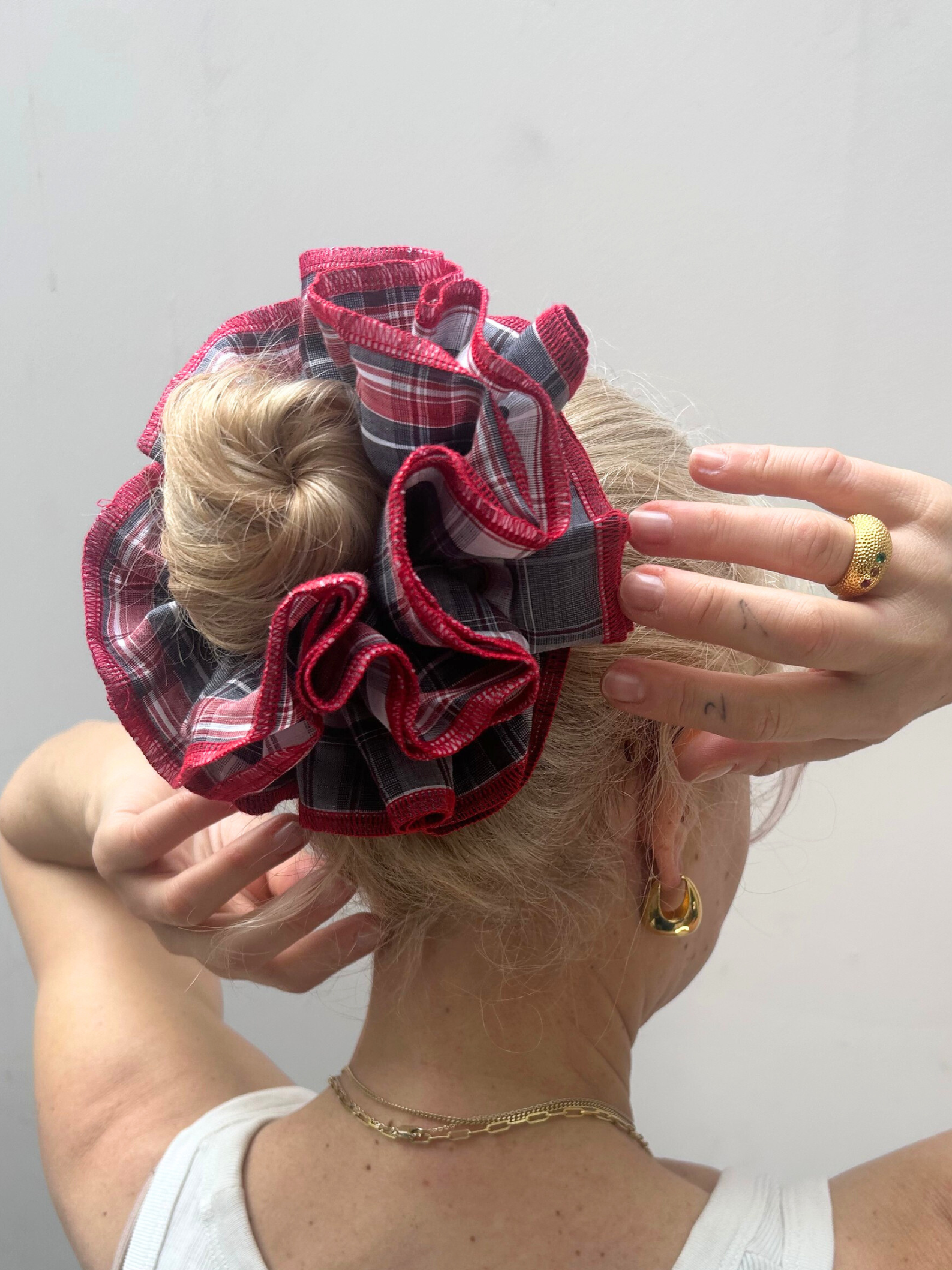 Person wearing a large plaid hair scrunchie on a plain background