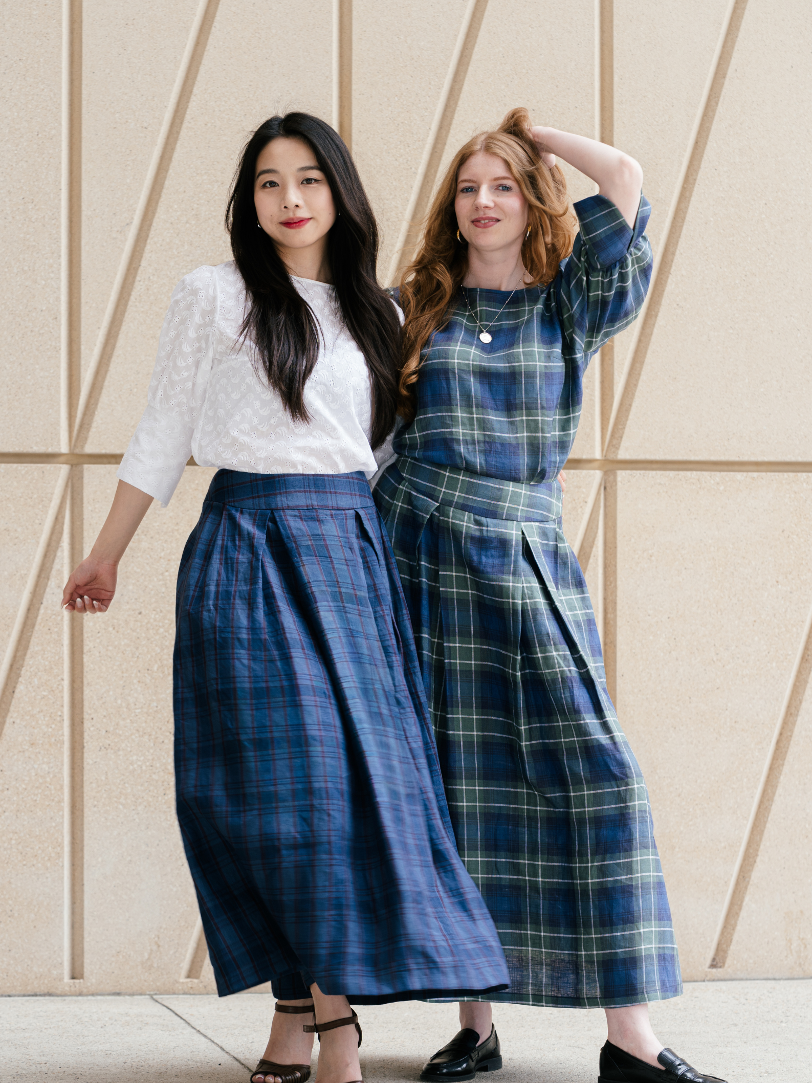 Two women wearing blue plaid dresses standing against a geometric-patterned wall.